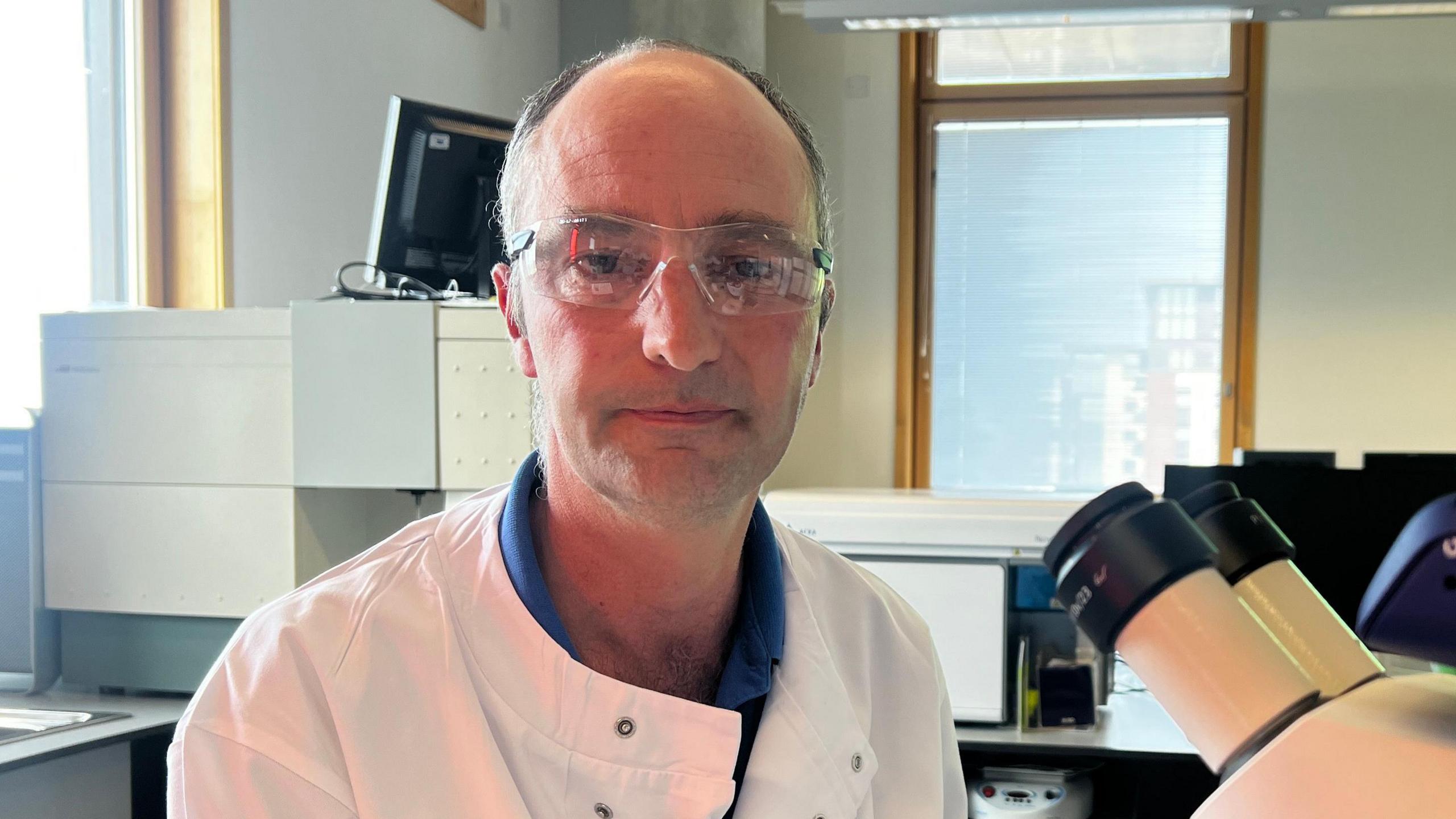 Dr Nick Tucker wearing a white lab coat in front of the twin eyepiece lenses