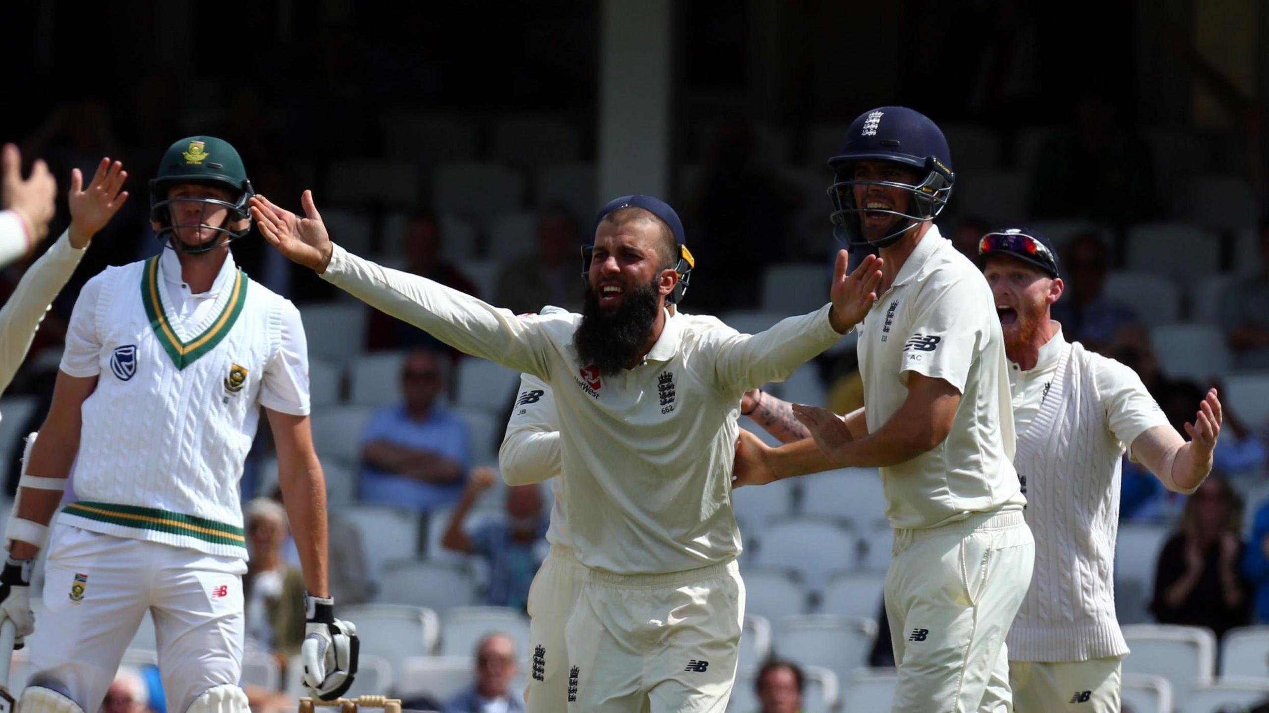 Moeen Ali next to Alastair Cook and Ben Stokes in cricket whites with his arms wide, appealing for a wicket