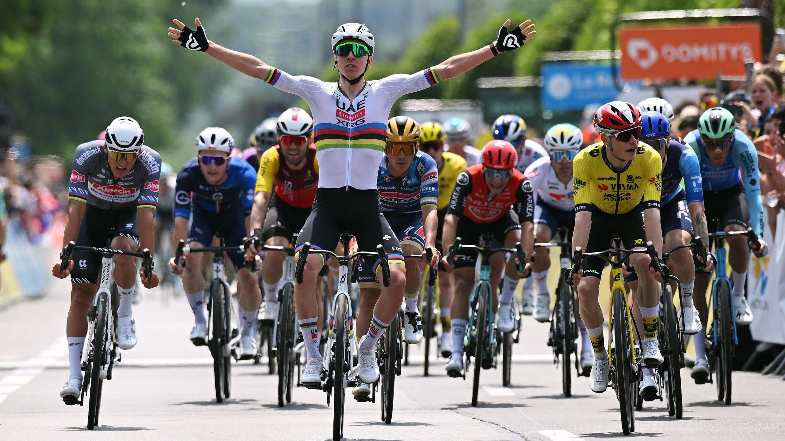 Tadej Pogacar celebrates with his arms outstretched as he crosses the line