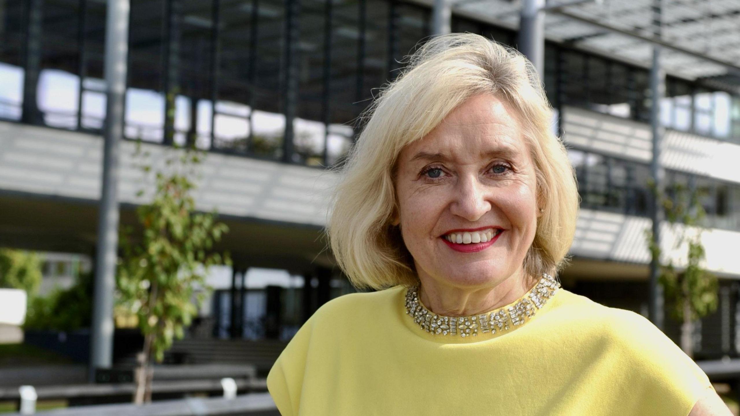 Professor Jenny Higham pictured smiling wearing a yellow top with a necklace around her neck