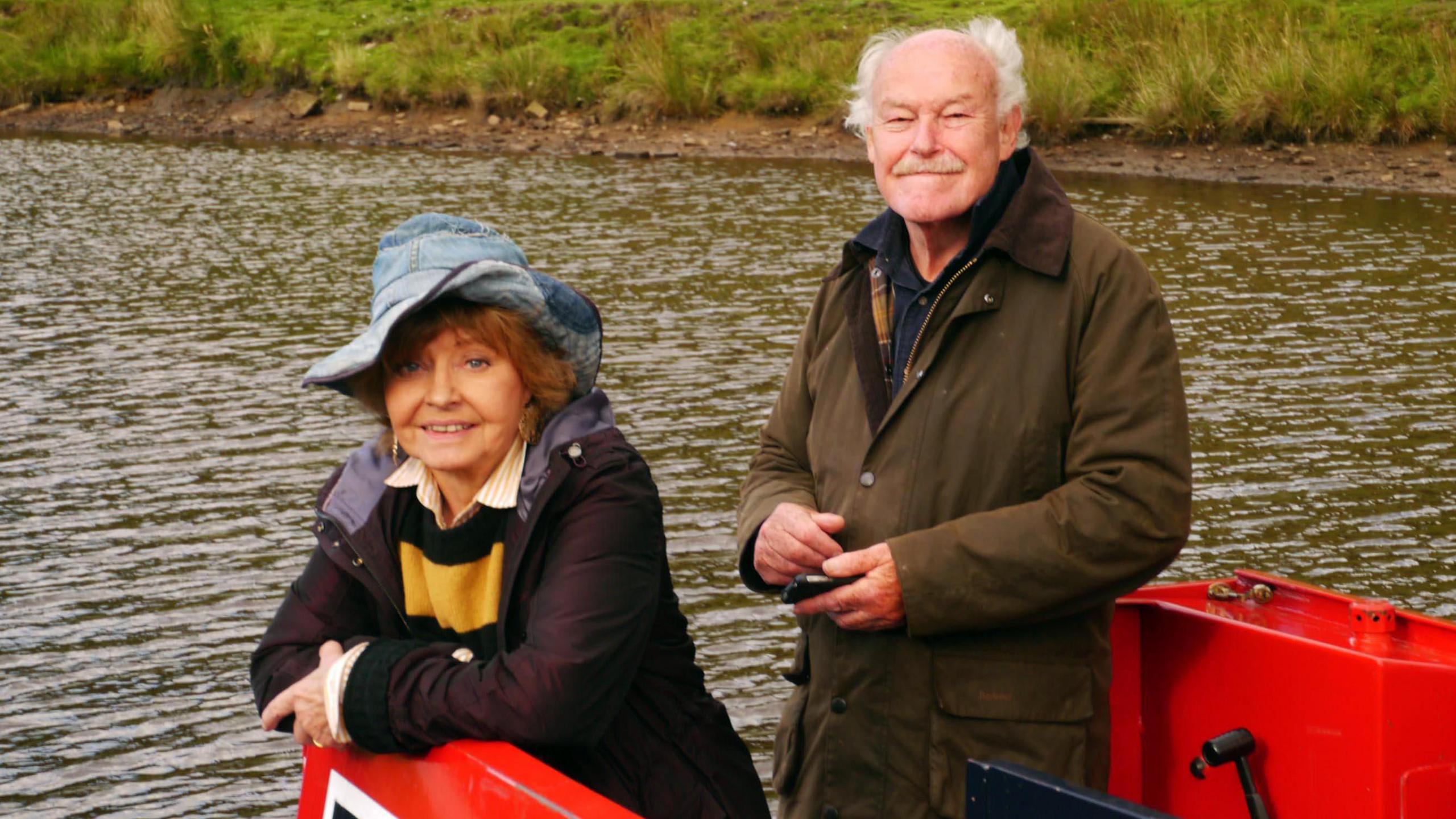 Prunella Scales and Timothy West in Great Canal Journeys. The couple are shown looking at camera from a lock on a canal.  Scales is wearing a floppy blue hat.