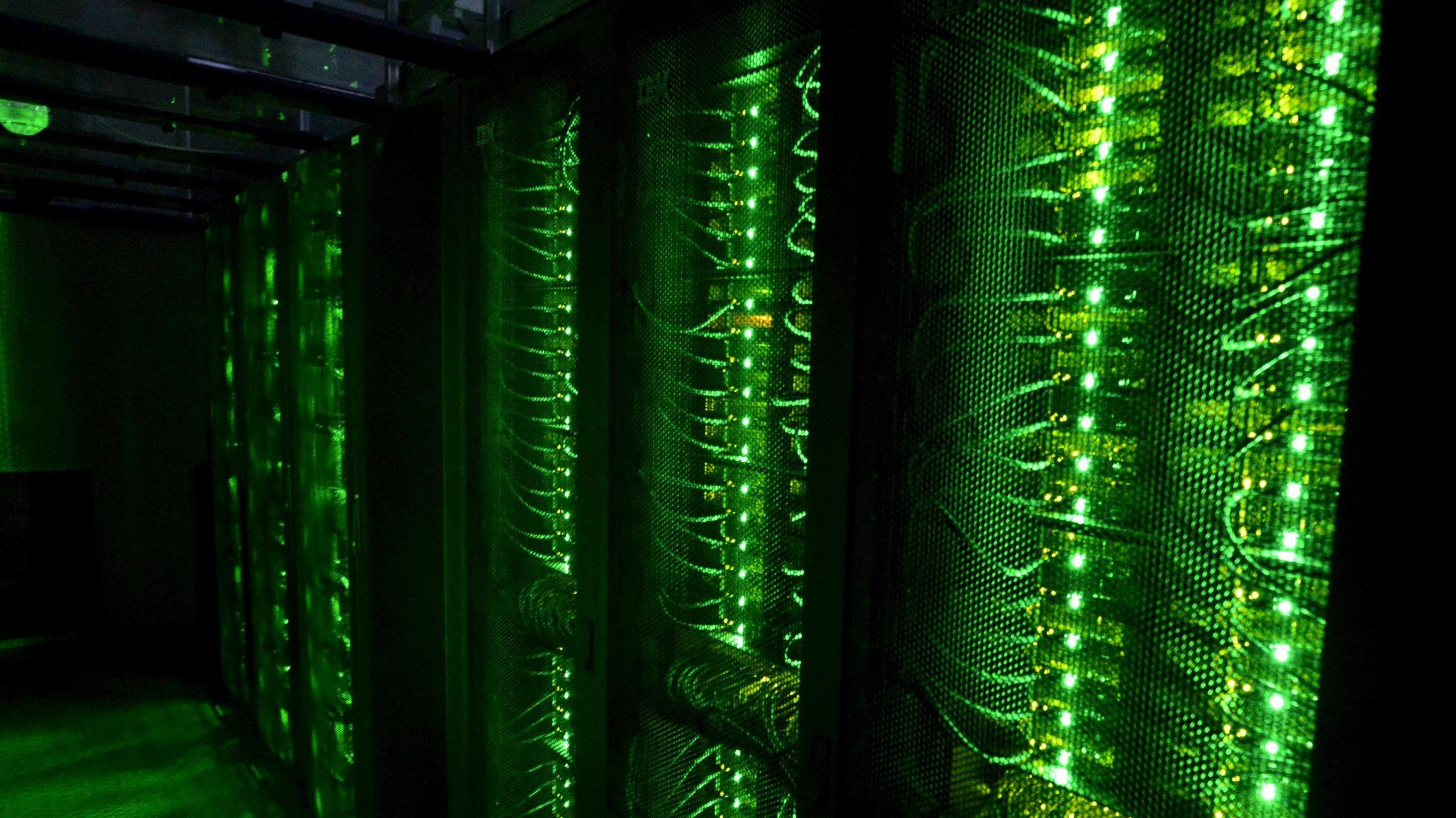 A bank of glowing green computer cables shine brightly against a deep black background in what is an unidentified data centre storage facility 