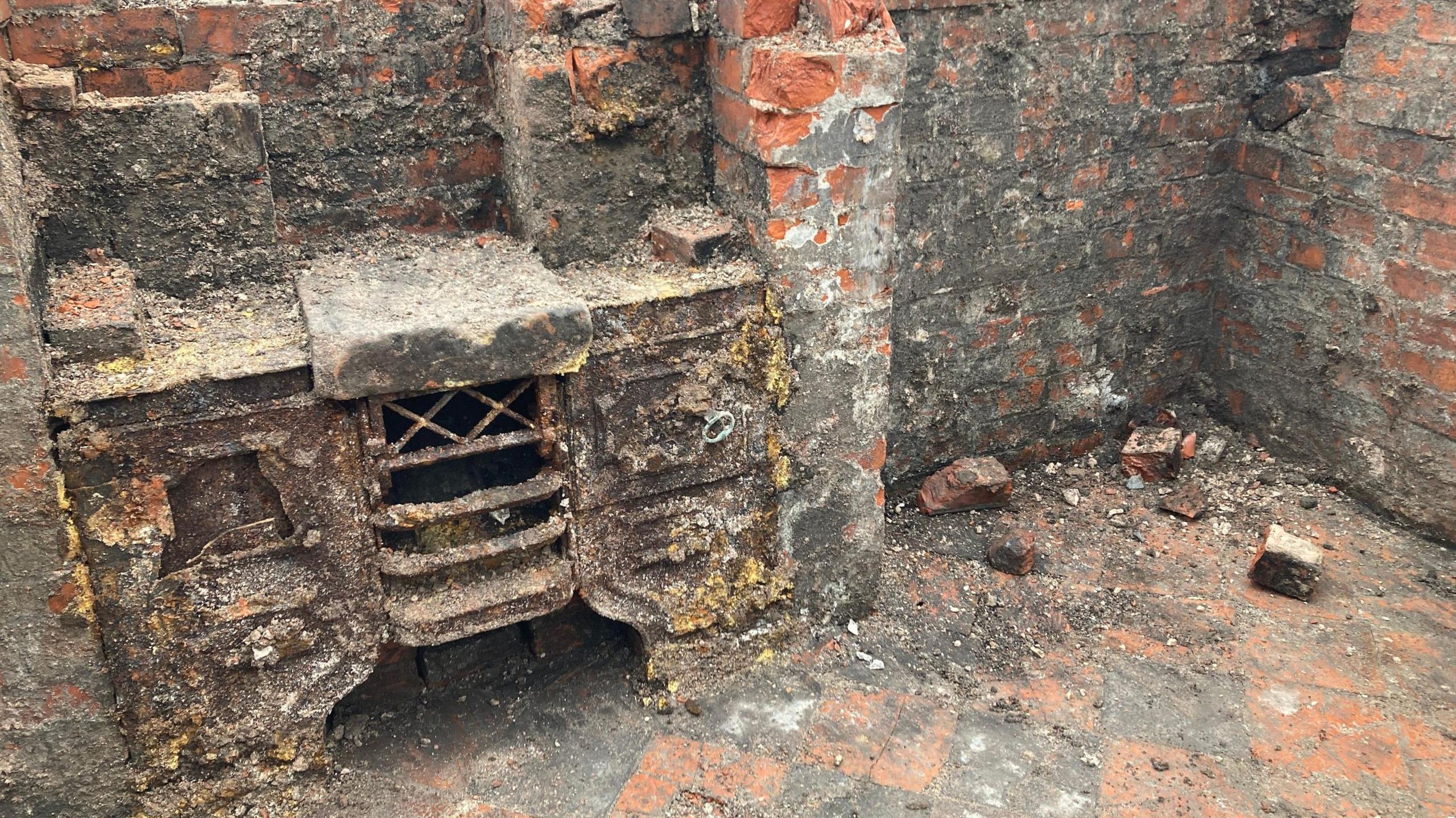 The remains of an old hearth, which is covered heavily in dirt and what appears to be moss. It is built in to a brick wall which is also very dirty