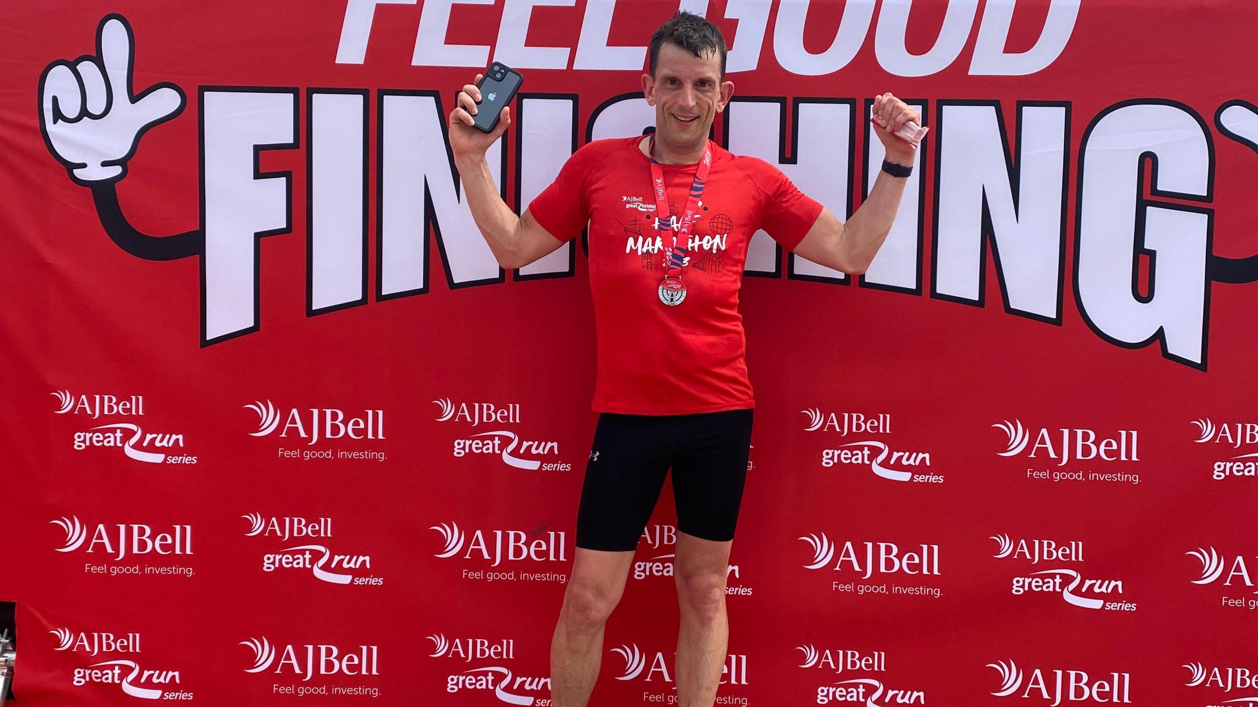 Rob with arms in air celebrating in front of red wall