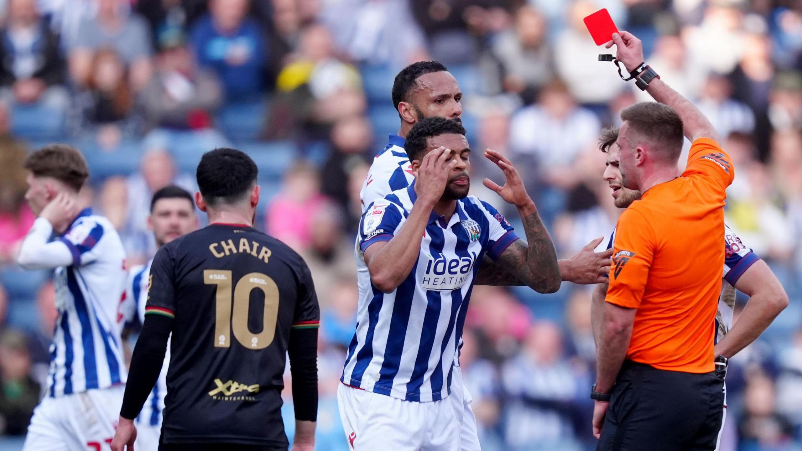 West Bromwich Albion defender Darnell Furlong puts his head in his hands as the referee holds a red card in the air