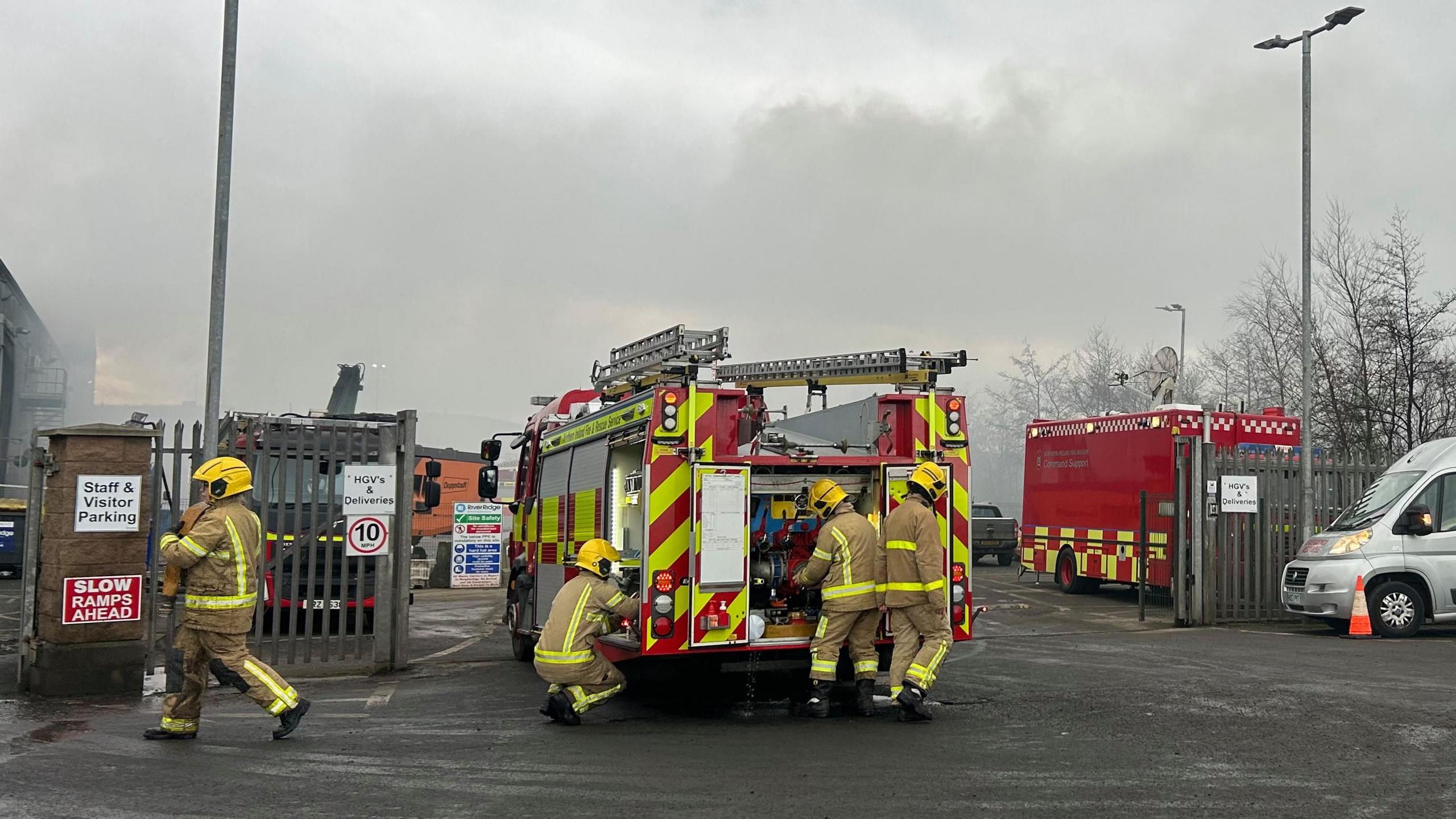 Firefighters around a fire appliance, smoke can be seen in the background. 