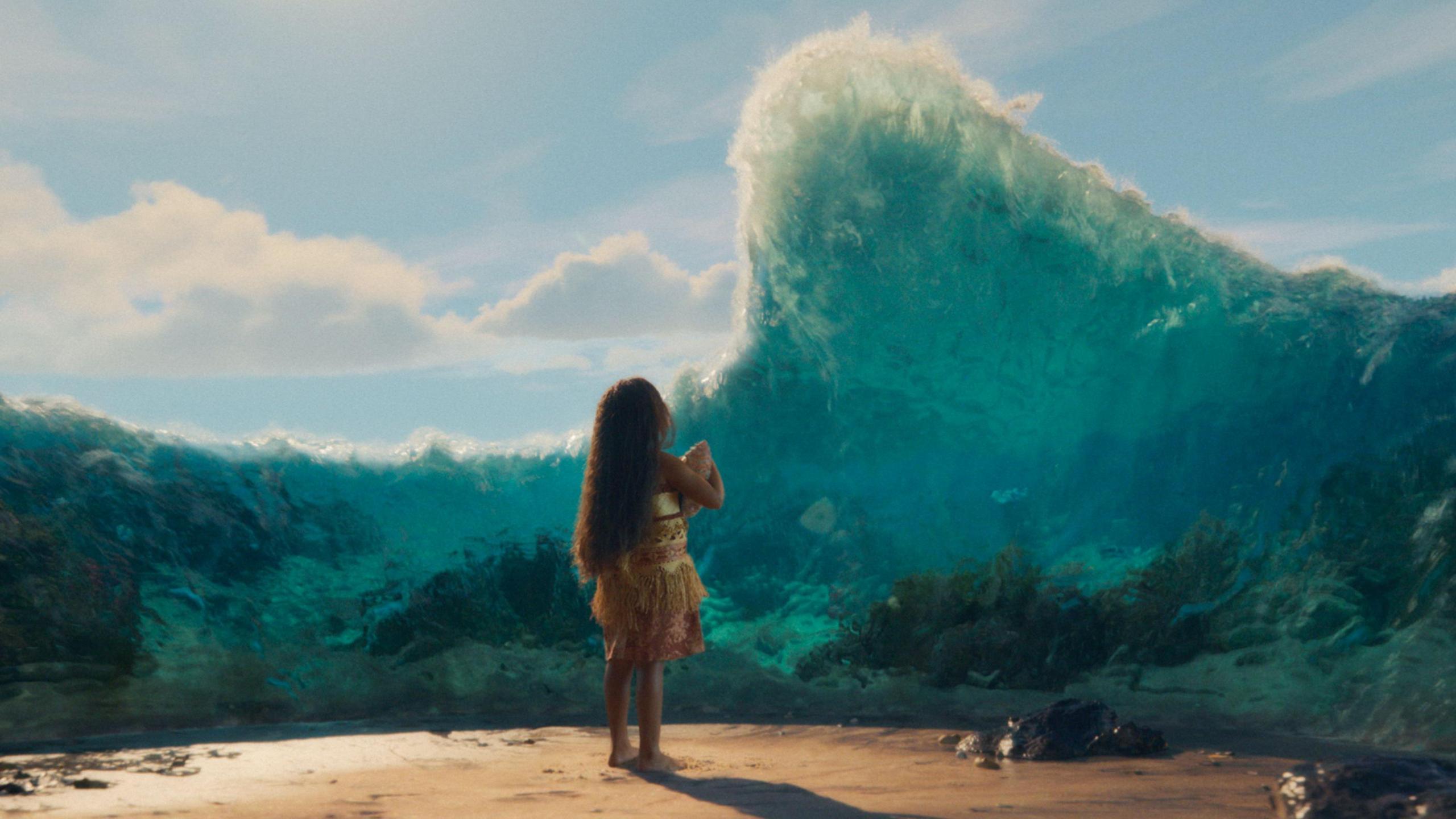 Moana is show as a young child facing away from the camera, surrounded by water that is lifting off the ground to form a wall in front of her. 