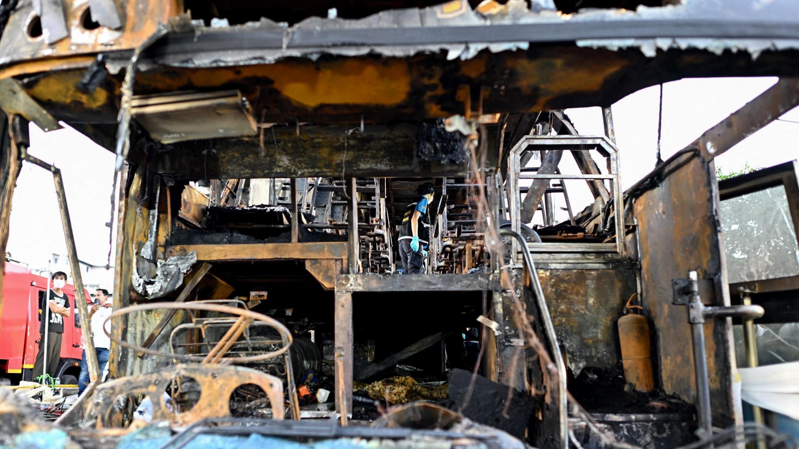 A police officer inspects a burnt-out bus that was carrying students and teachers on the outskirts of Bangkok on October 1, 2024. Rescuers pulled children's bodies from the charred wreckage of a Thai school bus on October 1 after an accident turned the vehicle into an inferno, with more than 20 feared dead.