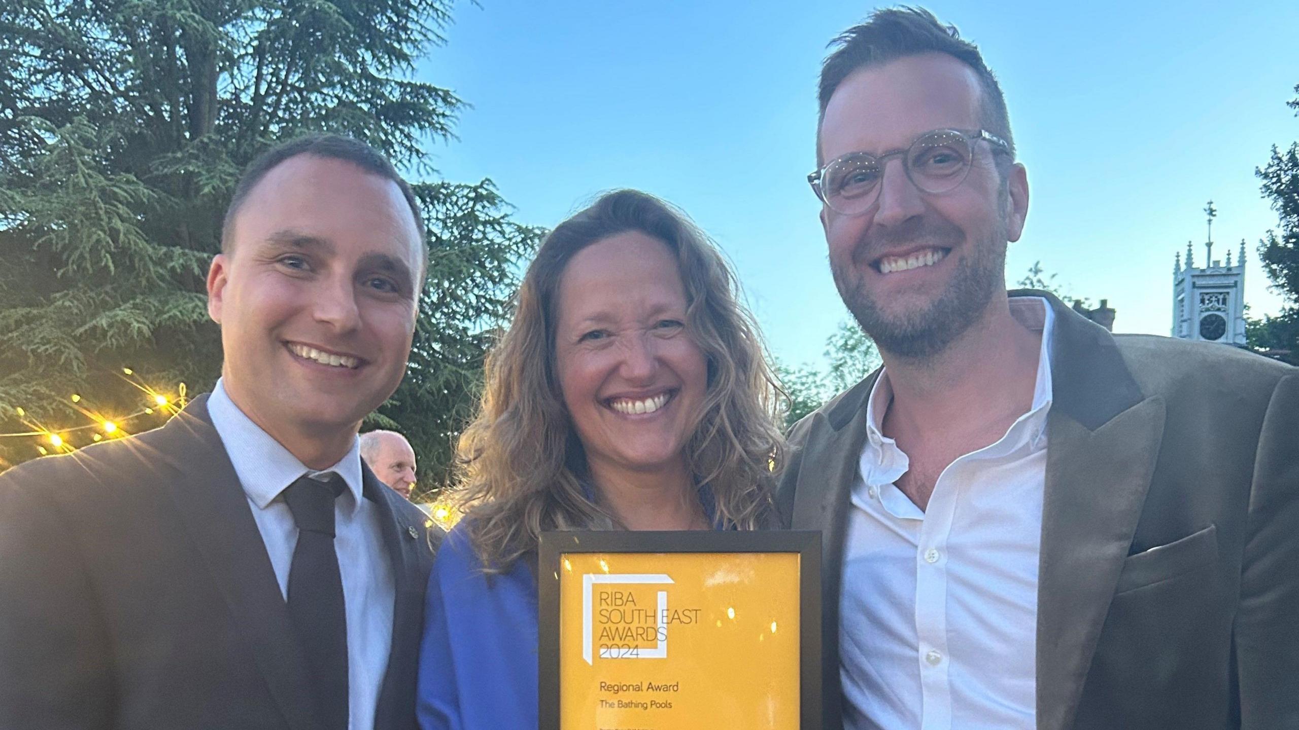 A woman and two men hold an award