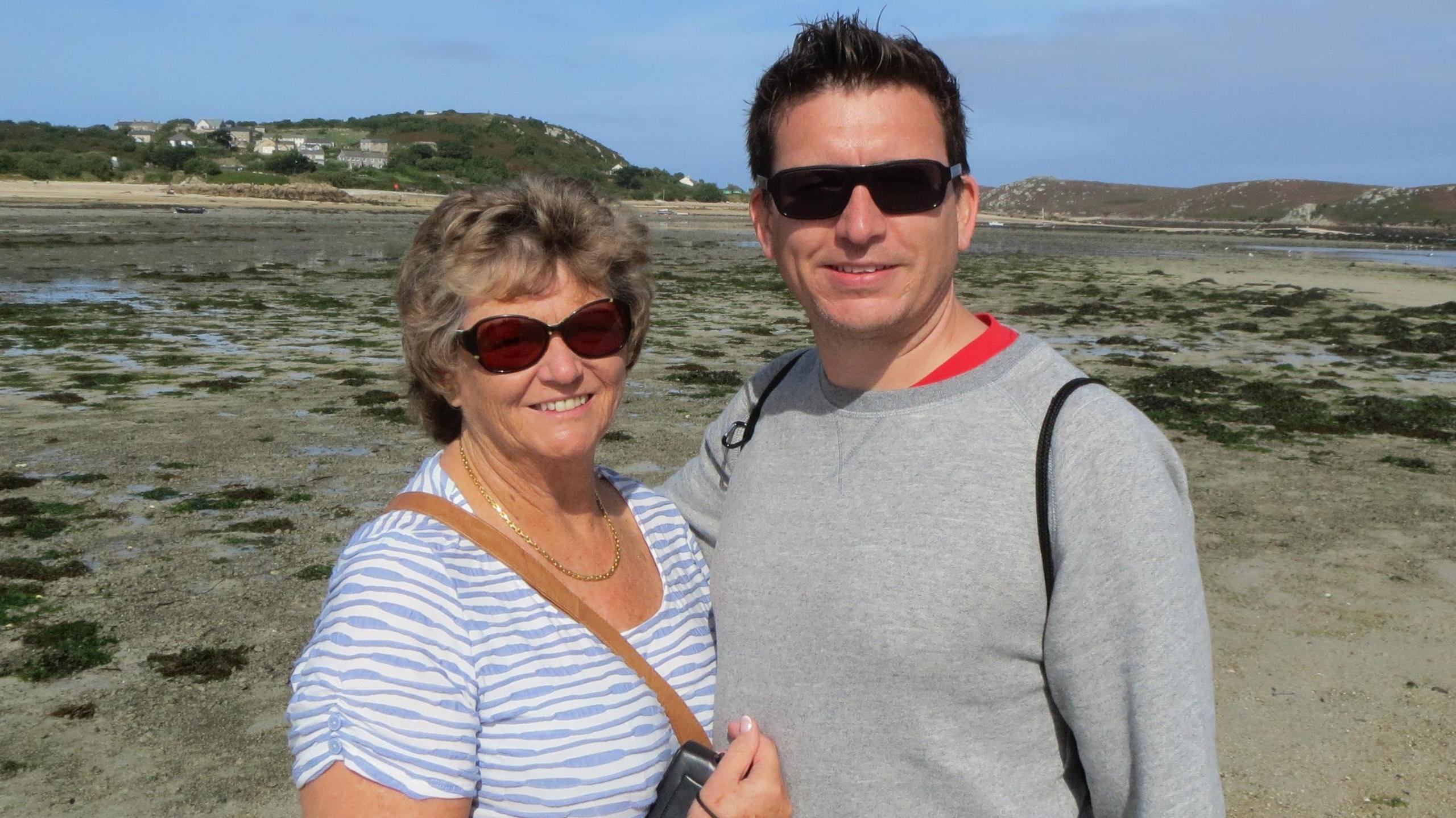 A man and woman posing for a photo on a beach with blue skies behind.