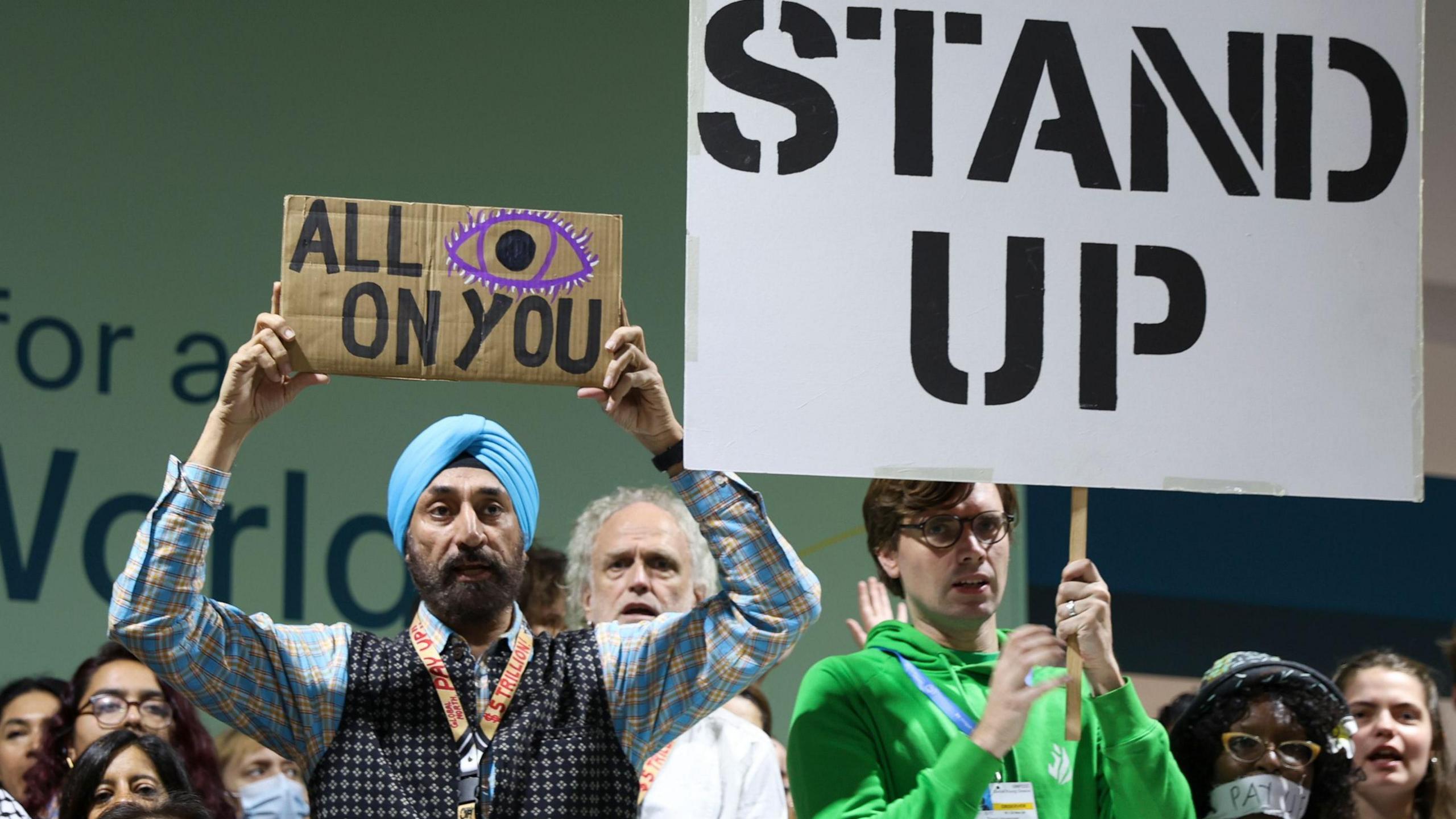 A group of protesters at the COP29 conference, with signs reading "all eyes on you" and "stand up"