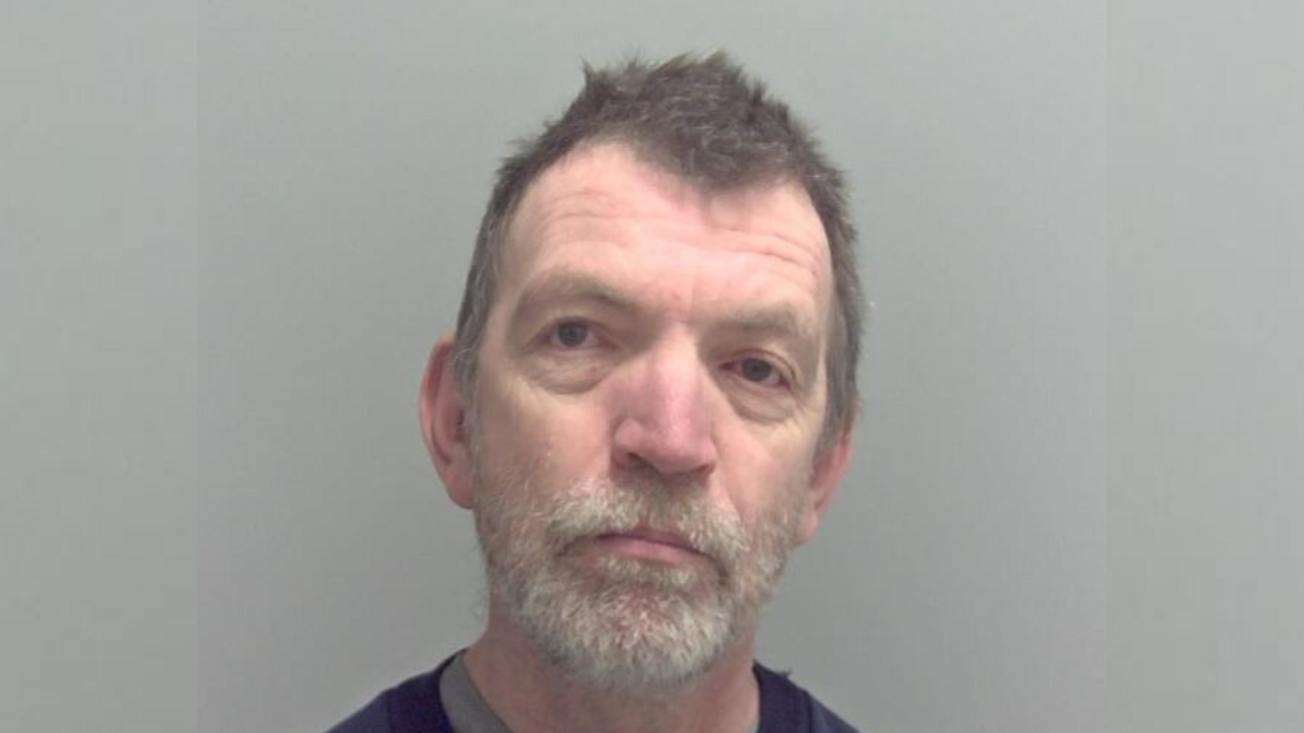 A police mugshot of Richard Cosburn  He has short brown hair and a grey beard.