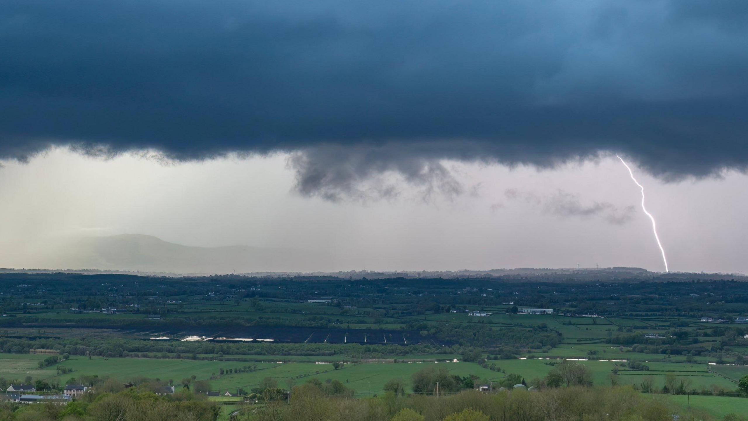 A lightning strike in the distance overlooking green fields