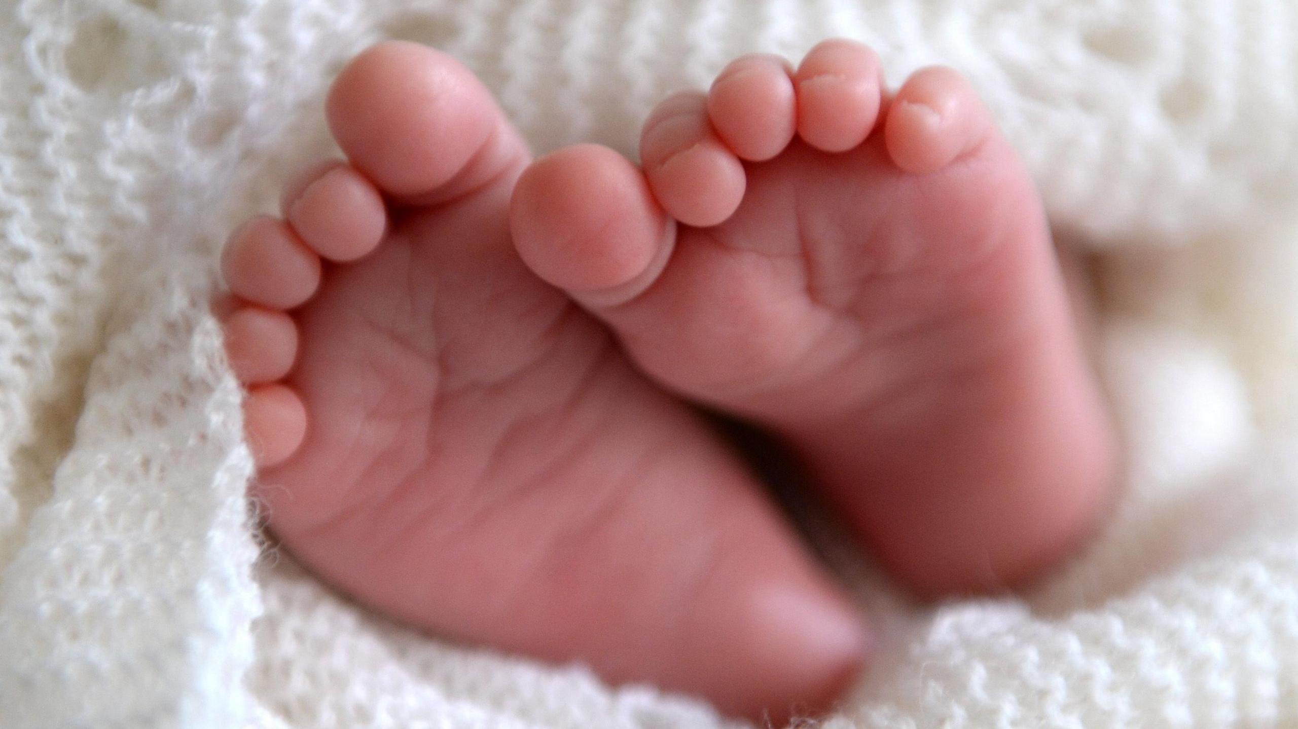 A newborn baby's feet poking out of a white knitted blanket.