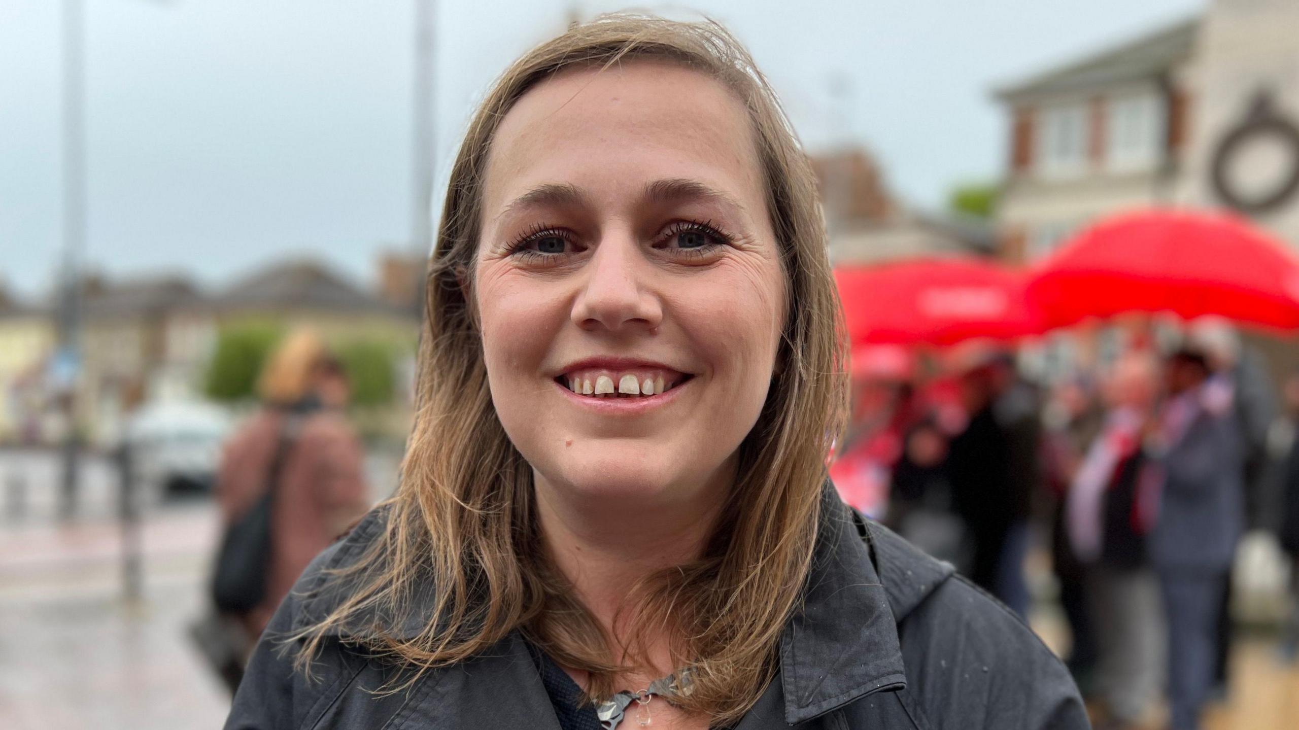 Jen Craft, with light brown hair, smiling at the camera. She is wearing a black coat while standing on the High Street