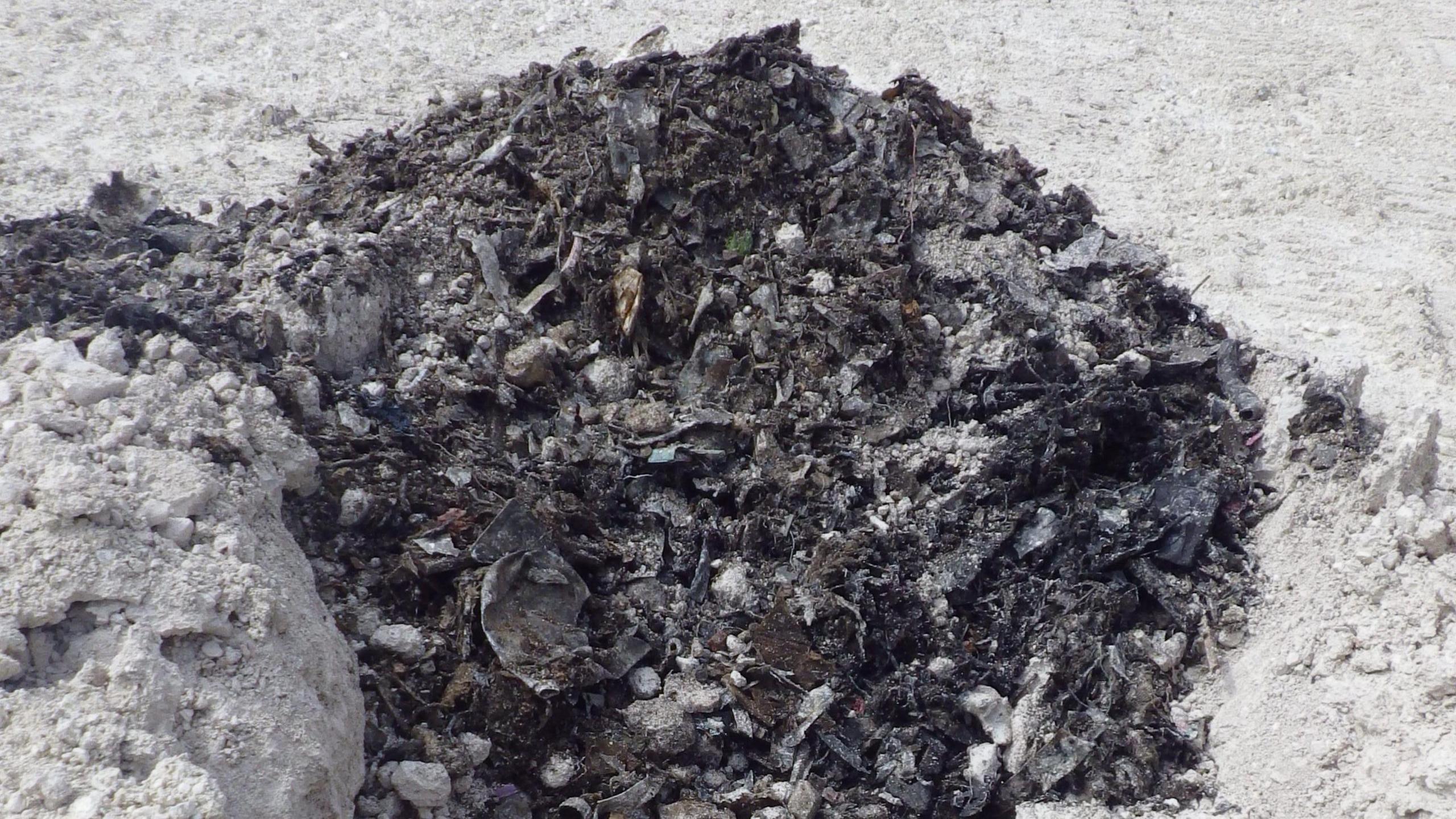 Illegally dumped waste in a quarry, that looks very dark, surrounded by chalk
