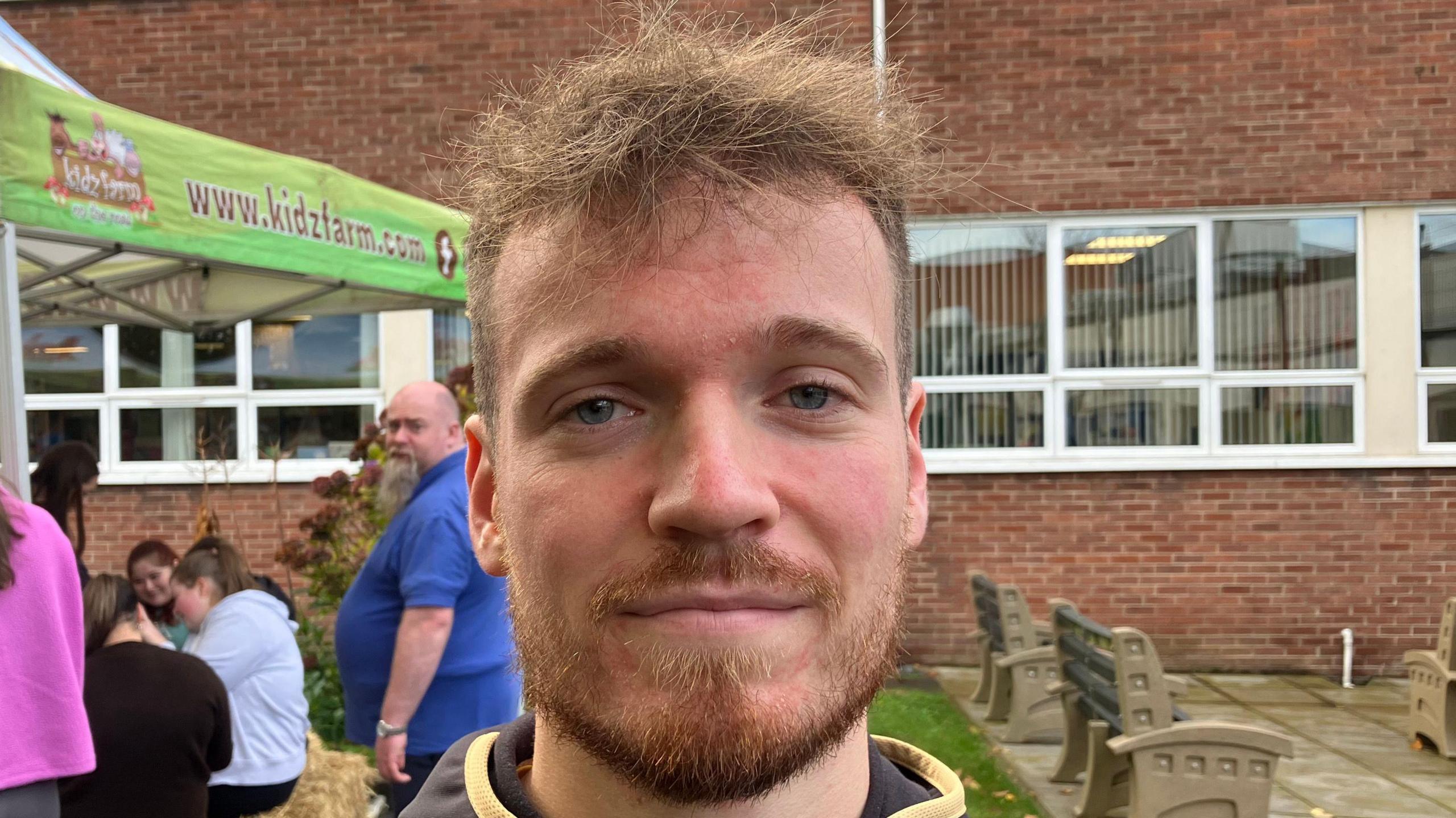 Caoilte Hamill pictured outside in a courtyard. He has short ginger/blonde hair and has a giner/blonde beard. He is wearing a black tracksuit top.