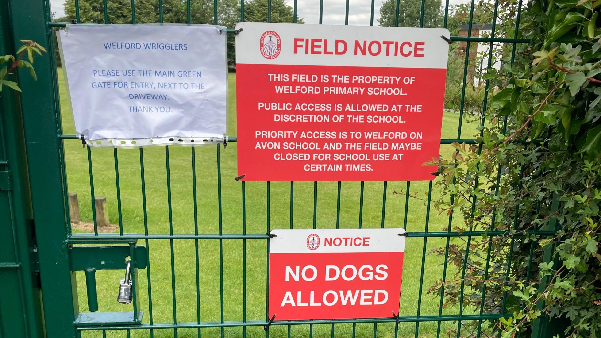 A green school gate with signs on that the field beyond is closed to the public