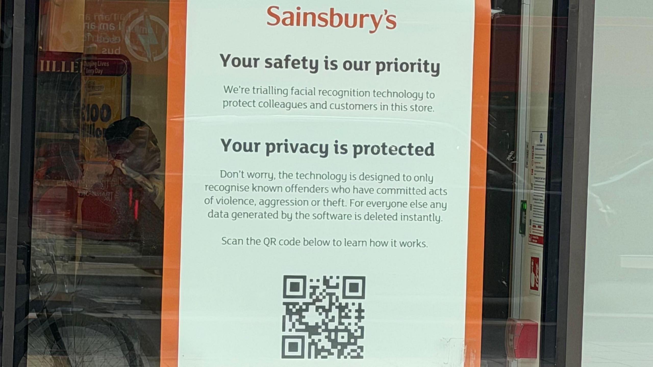 A Sainsbury's poster in a store's front window, outlining its use of facial recognition technology, above a QR code.