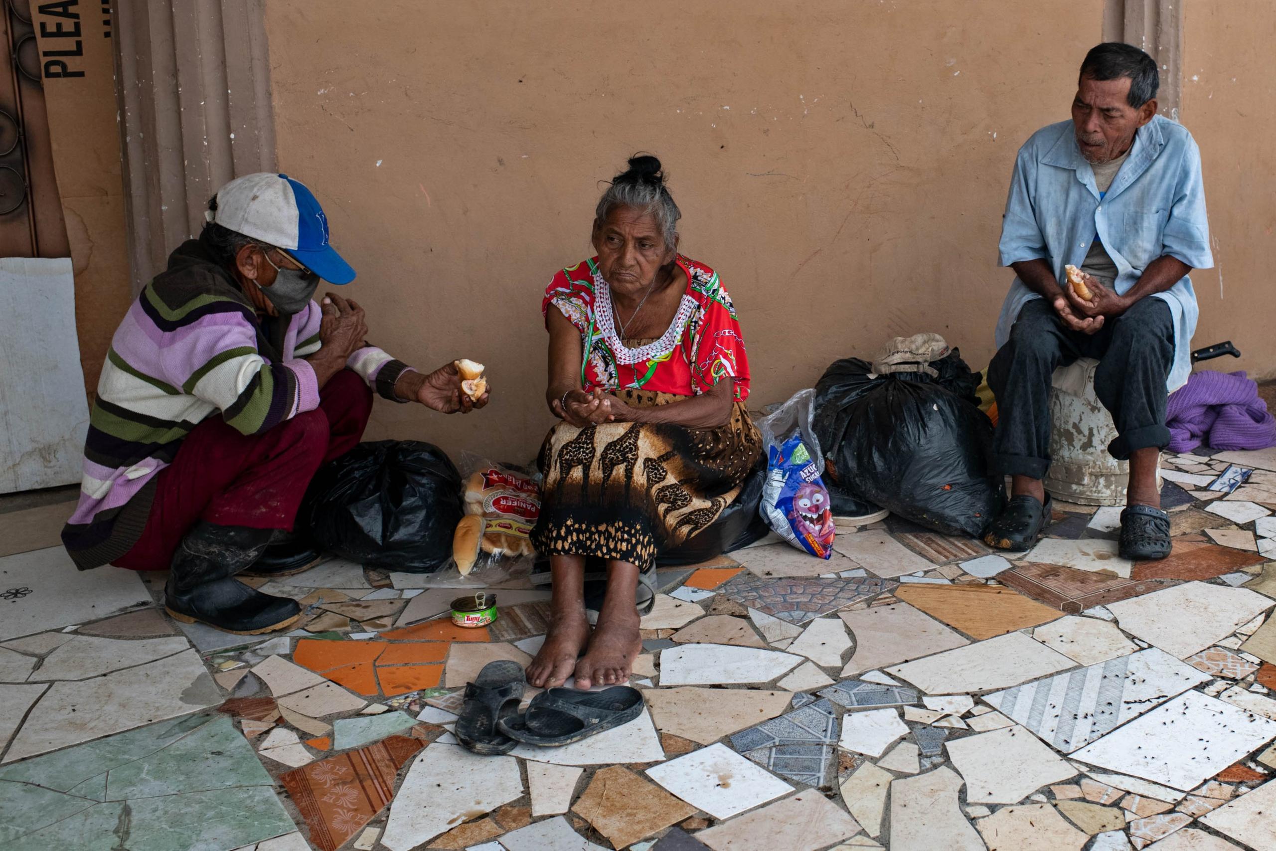 Gloria sits on the floor while a man offers her some fruit to eat