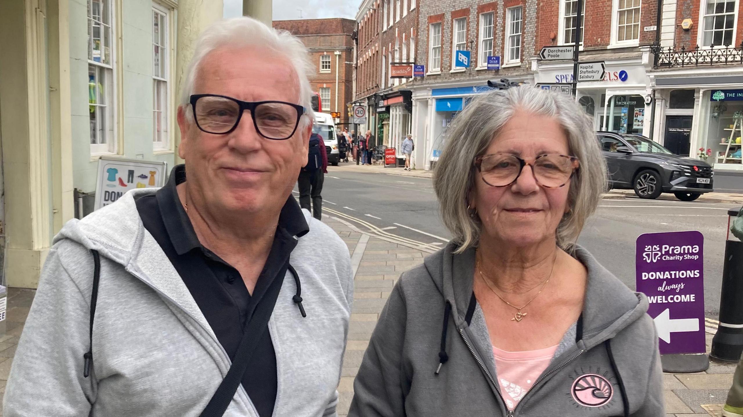 A man and woman being interviewed on the street. They are both wearing grey hooded tops