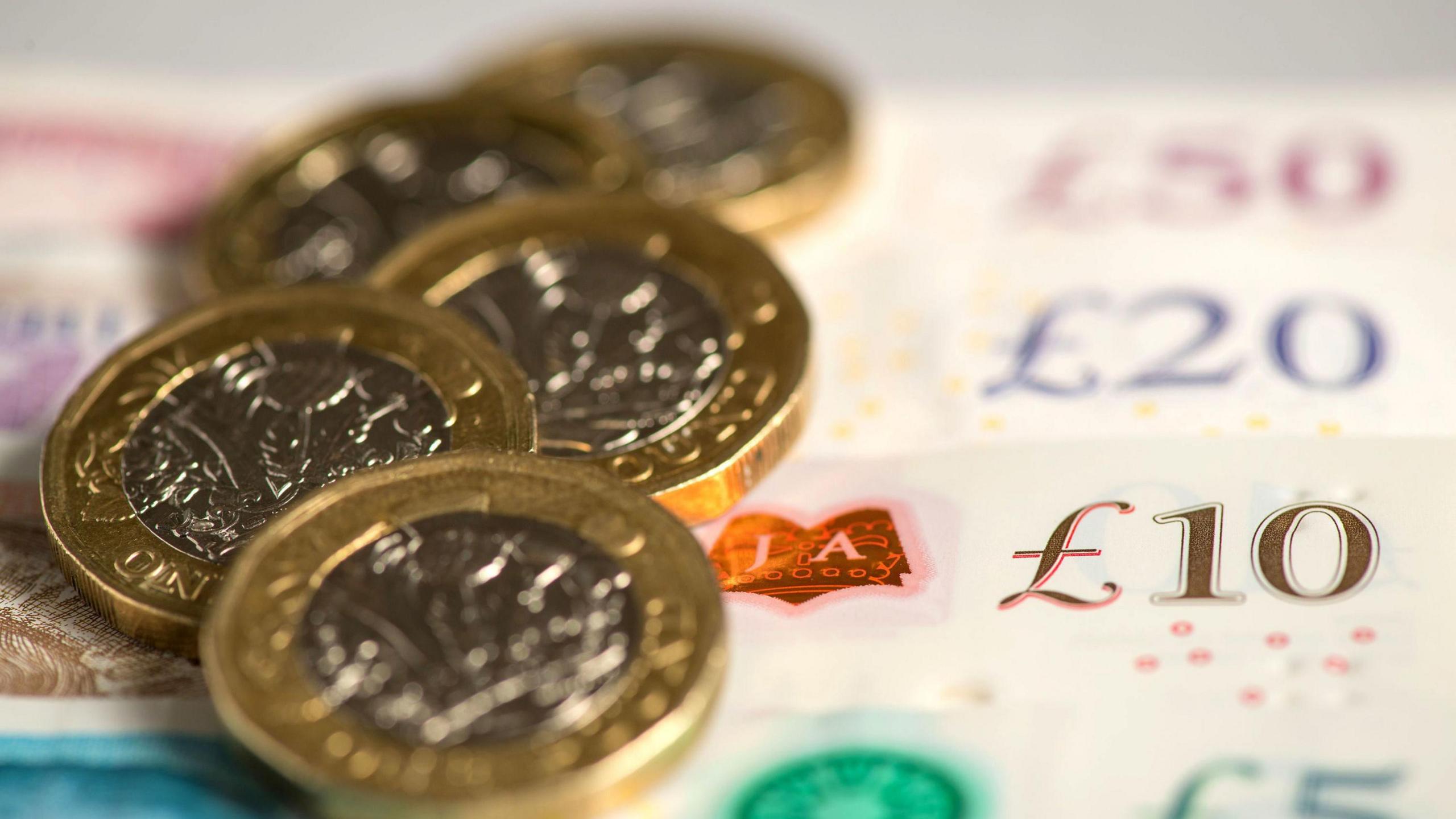 Close-up of a £5, £10, £20 and £50 note laid on a table. Pound coins are laid next to it.