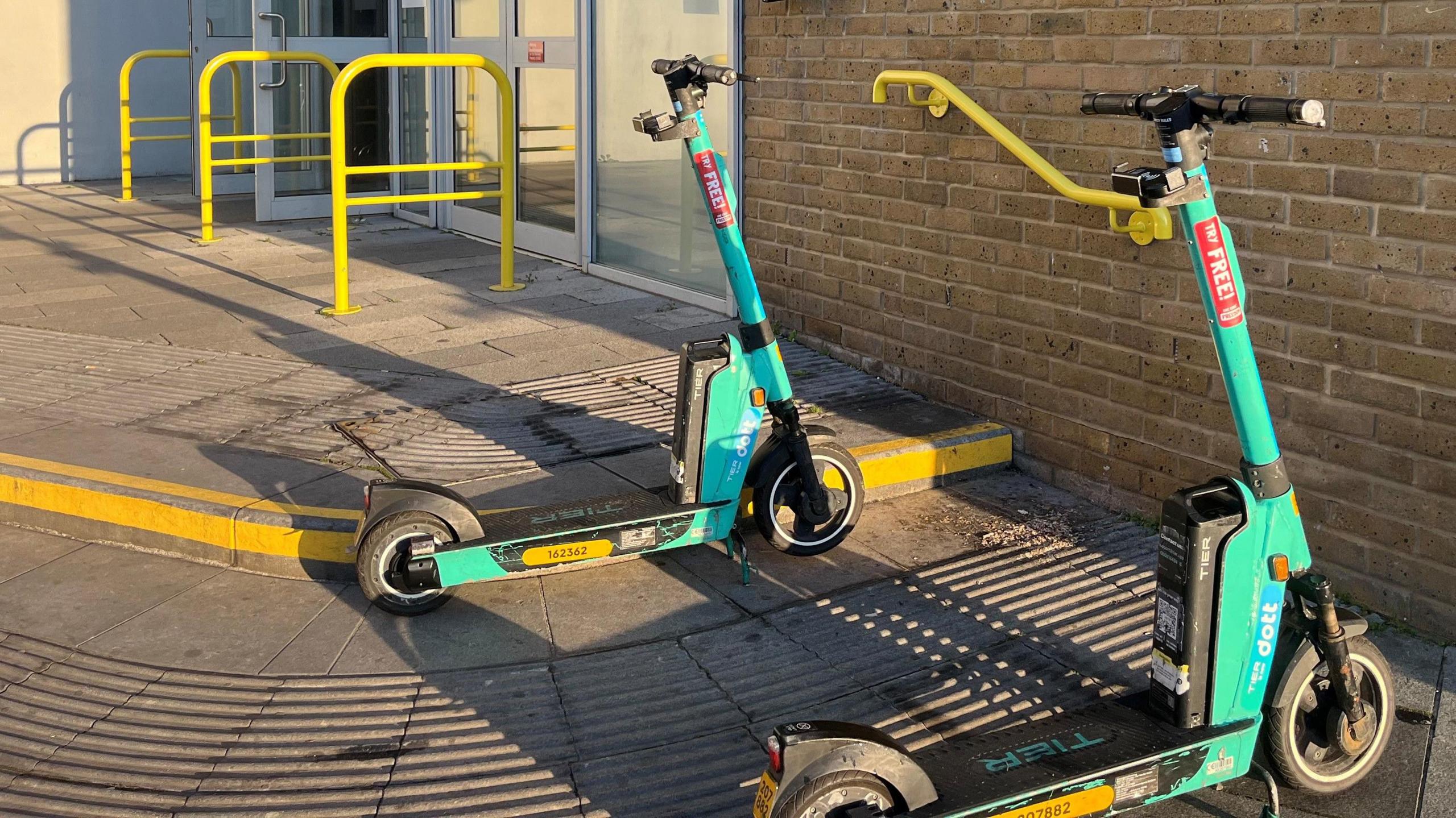 Two green Dott e-scooters parked outside Chelmsford railway station.