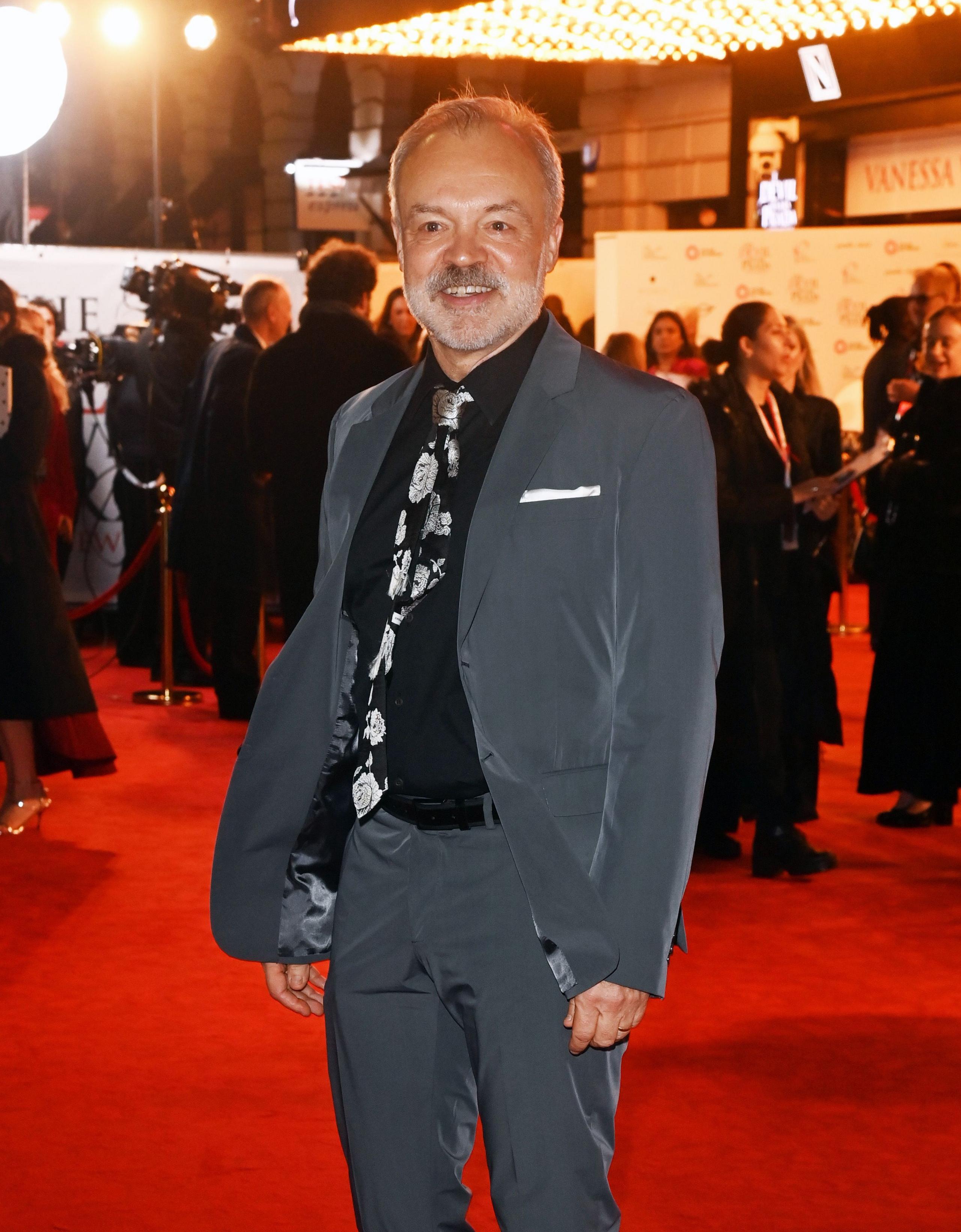 Graham Norton wears grey suit and black shirt on red carpet of Devil Wears Prada: The Musical