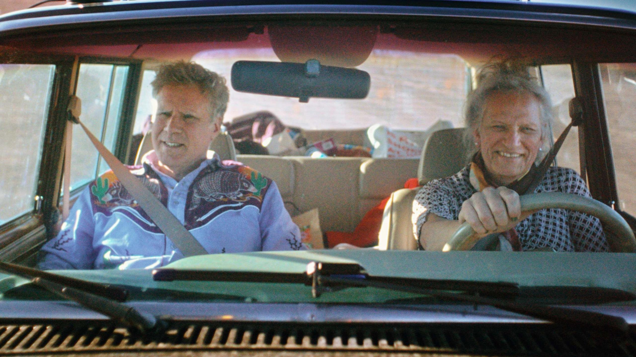 Will Ferrell and Harper Steele in a car that Harper is driving. He is wearing a blue cowboy shirt and she is wearing a black gingham top