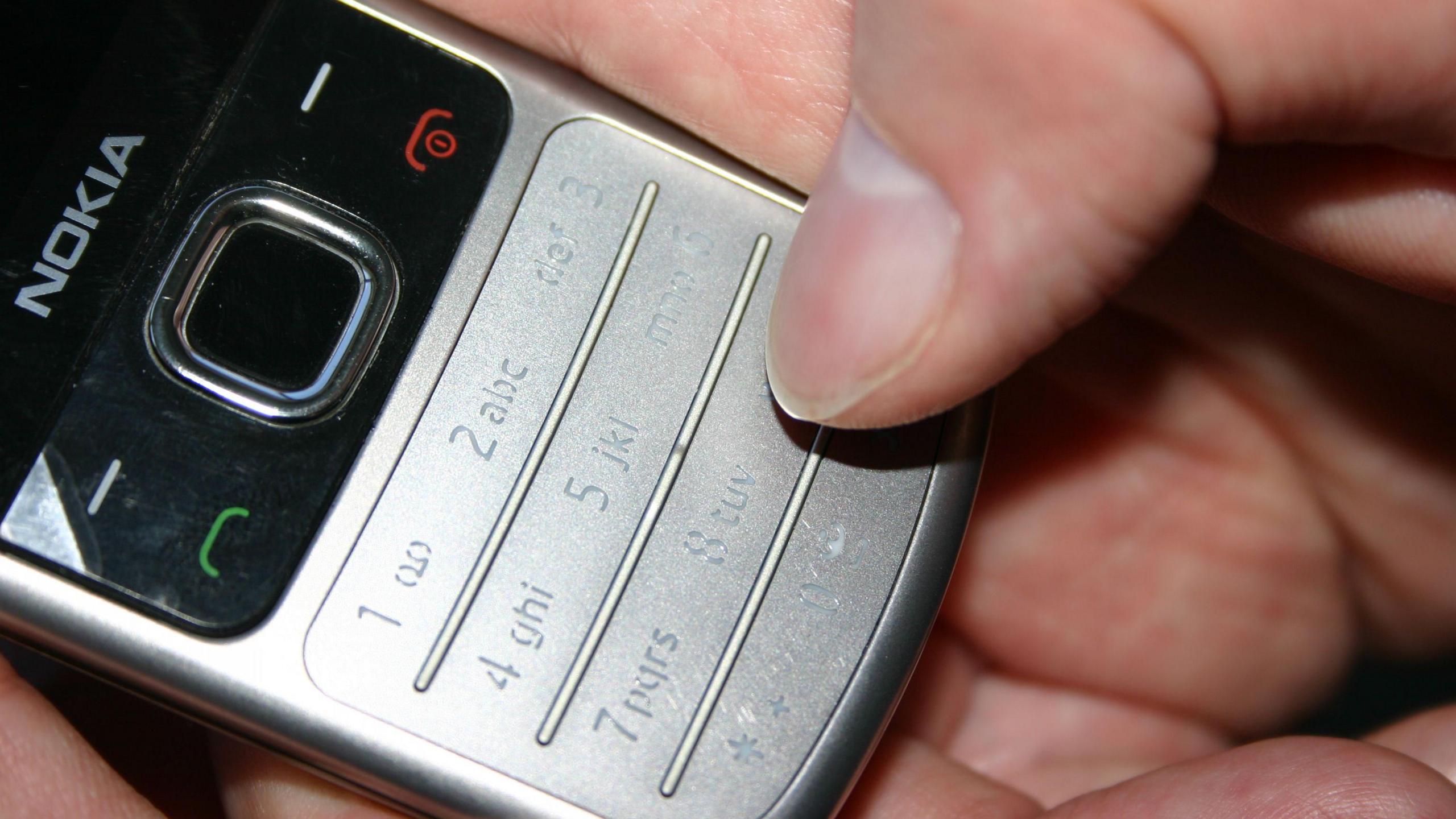 An old silver Nokia mobile phone with a person's thumb on the number 9.