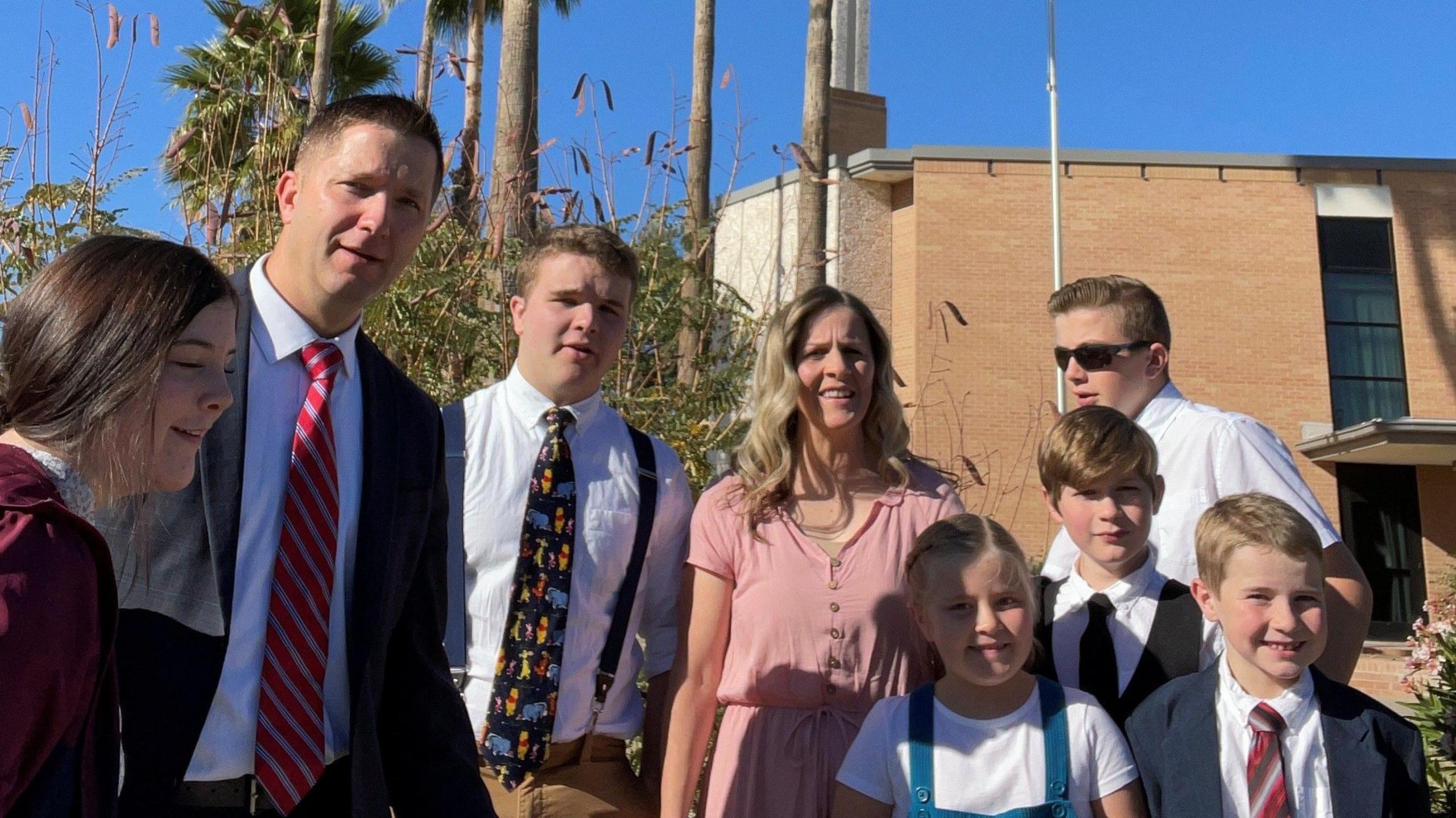 A man and woman standing outside a church with their six children. They are all smartly dressed.