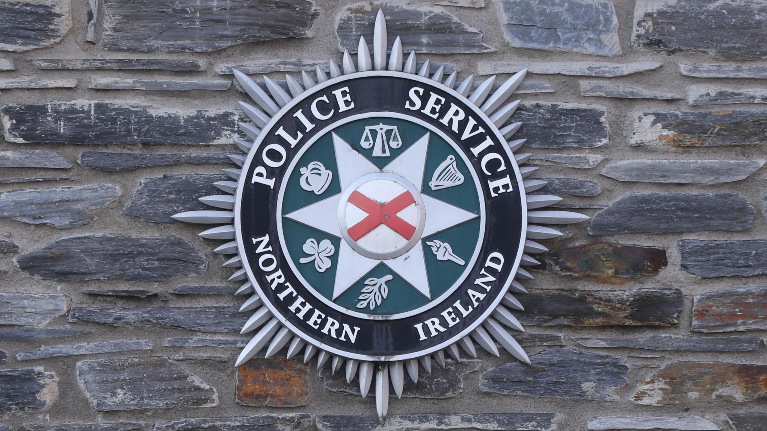 A PSNI badge on a grey brick wall.