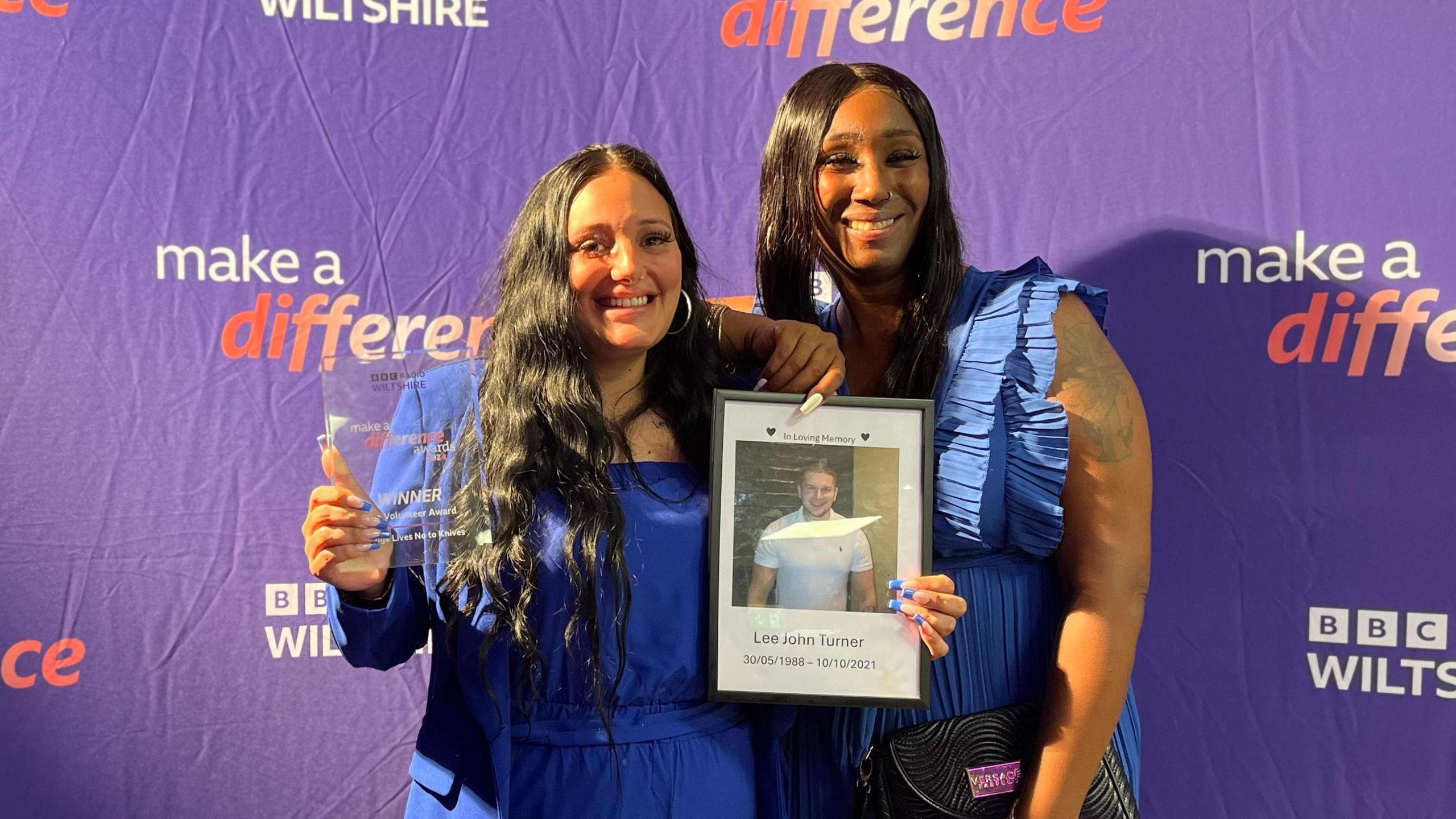 Jordan Turner and Danyelle King hold the award together in front of a BBC Wiltshire banner and a photo of Jordan's brother