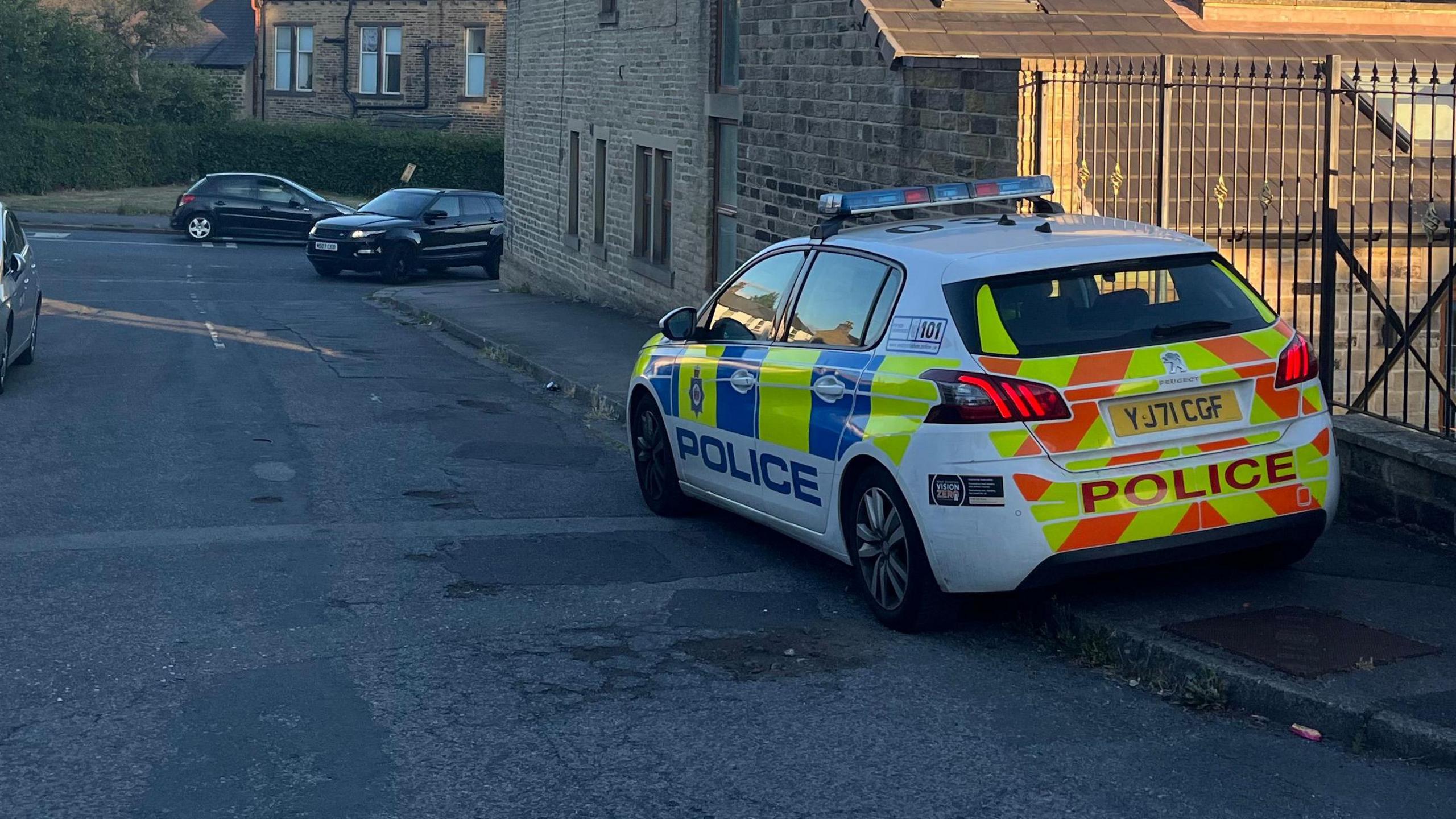 A police car is parked on the pavement alongside an iron fence.