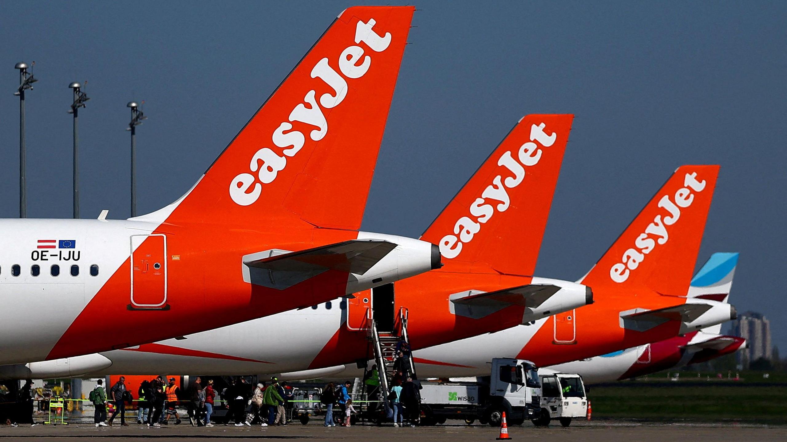 Three EasyJet planes lined up at an airport, with the focus on the orange tails of the planes, which have the word easyJet in white.