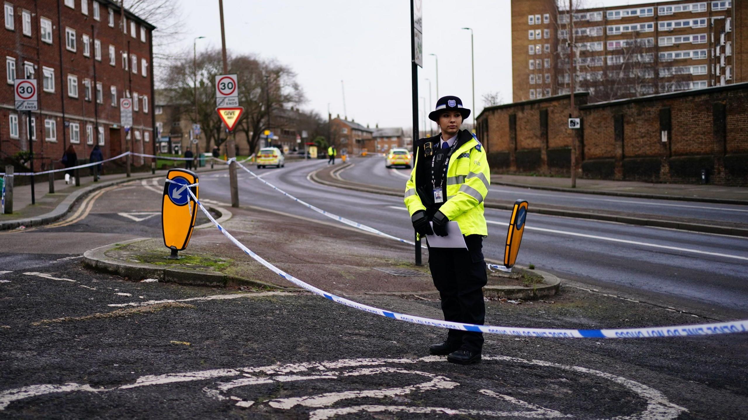 A female police officer standing in front on police tape on Woolwich Church Street 