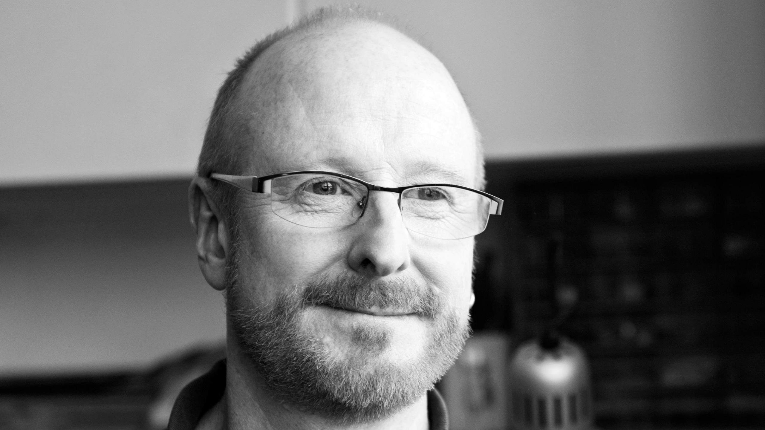 A black and white photograph of a man with a beard wearing glasses.