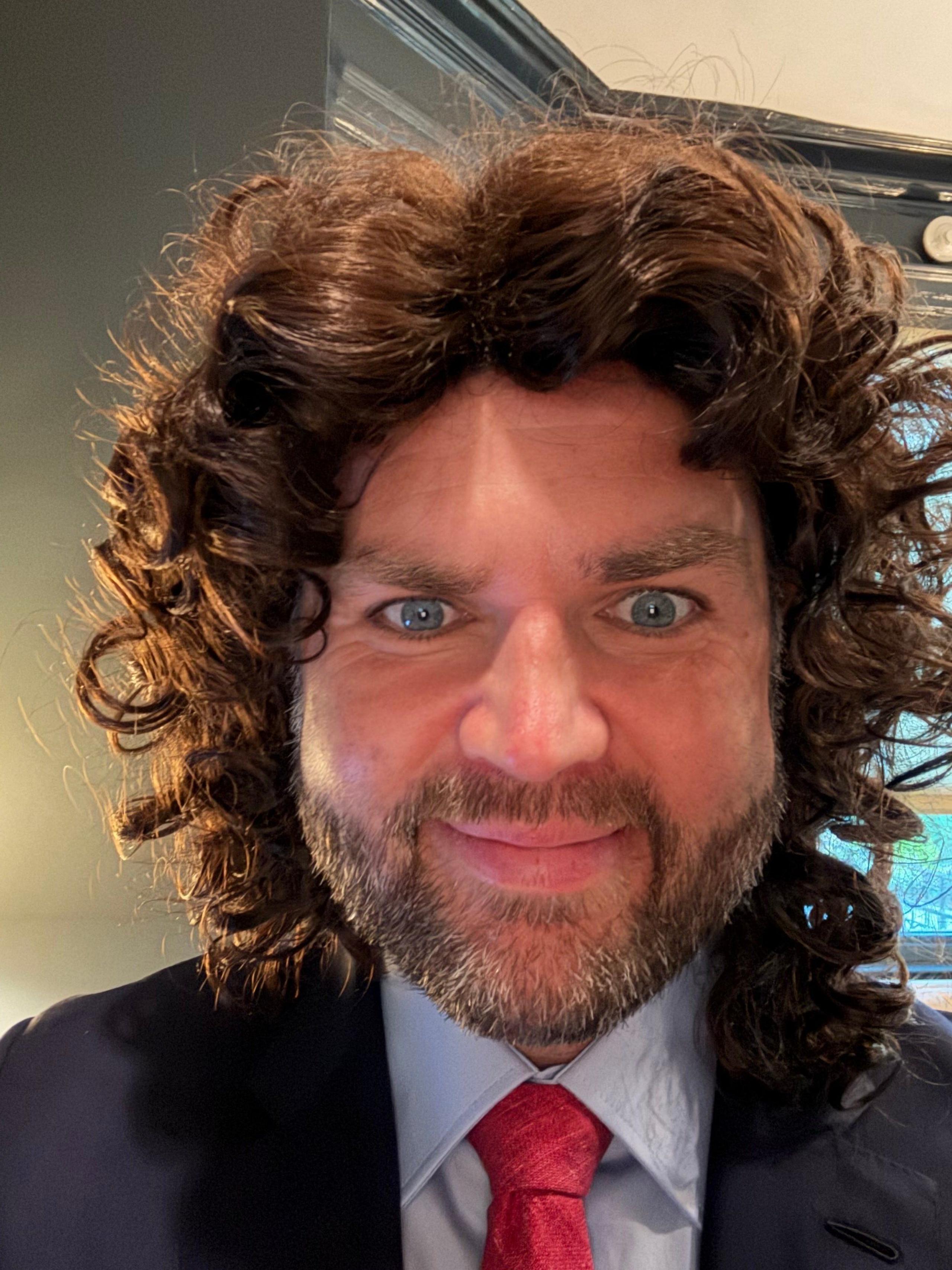 JD Vance in a wig and suit with his eyes wide open