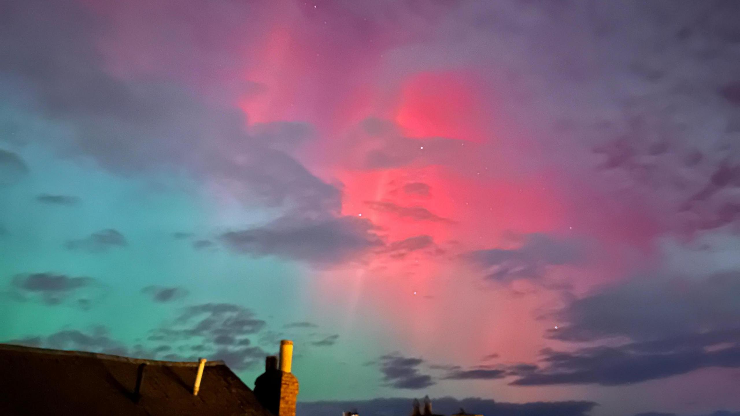 The sky was blue and pink. There is also clouds within the sky. A rooftop can be seen at the bottom of the picture.