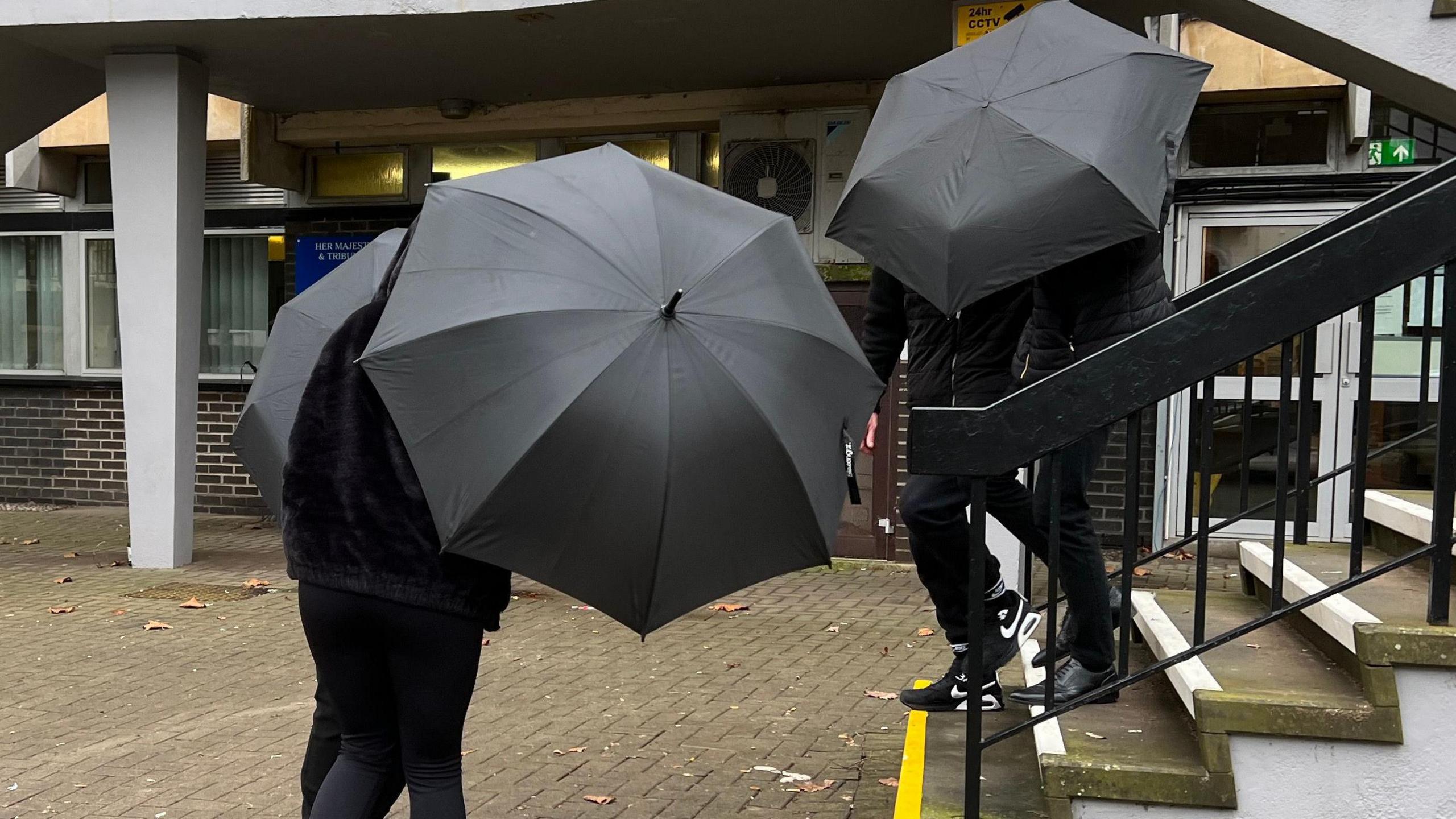 Four people wearing black under black umbrellas