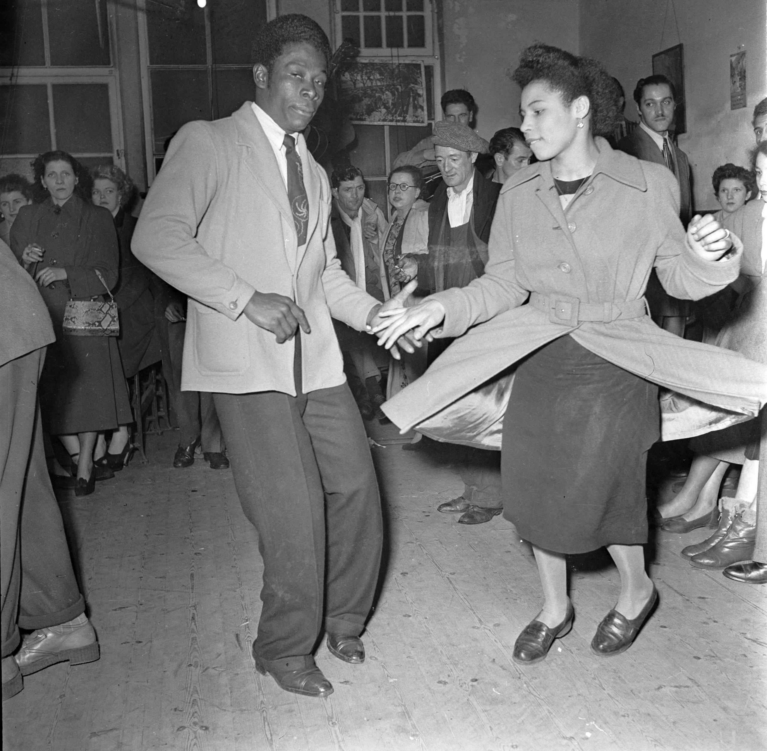 A young couple jiving surrounded by onlookers.
