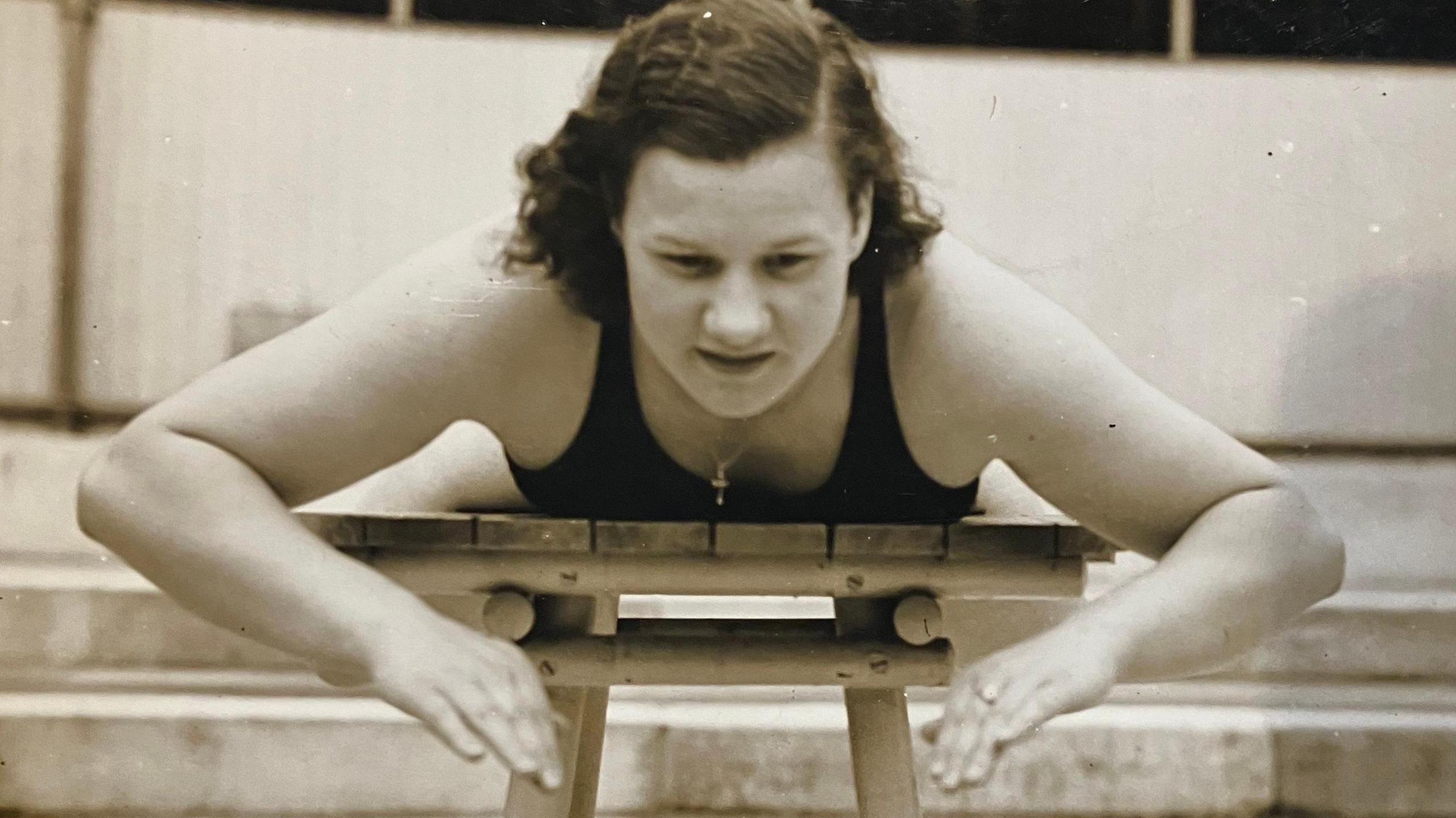 A 1930s black and white picture of a woman lying in a wooden table practising her breaststroke. 