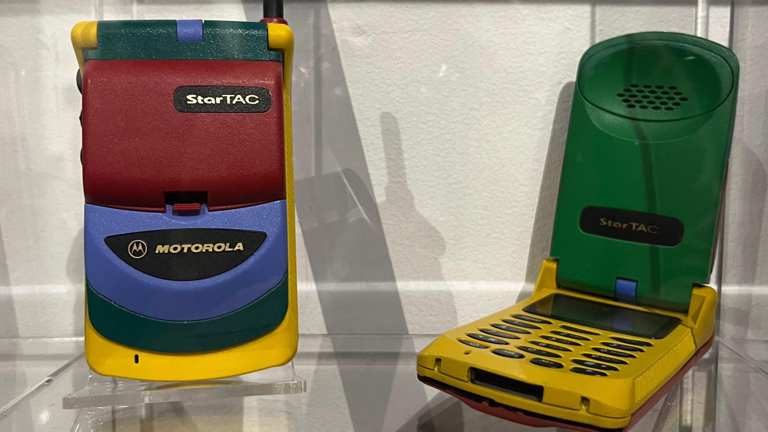 Two old mobile phones - one is a Motorola blue maroon and yellow flip phone in a 