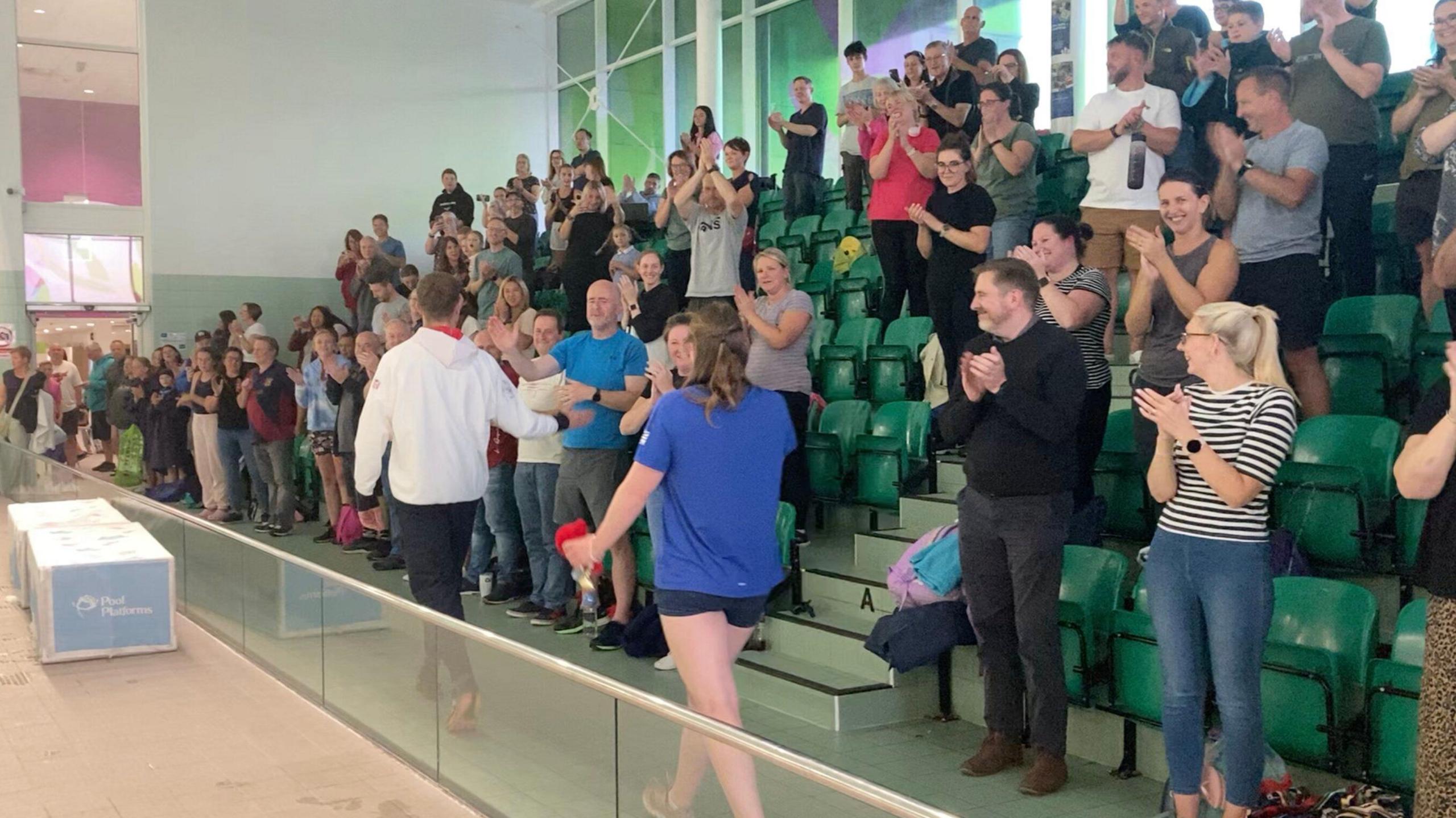 Matt Redfern and Becky Redfern walk in front of a cheering gallery of people clapping 