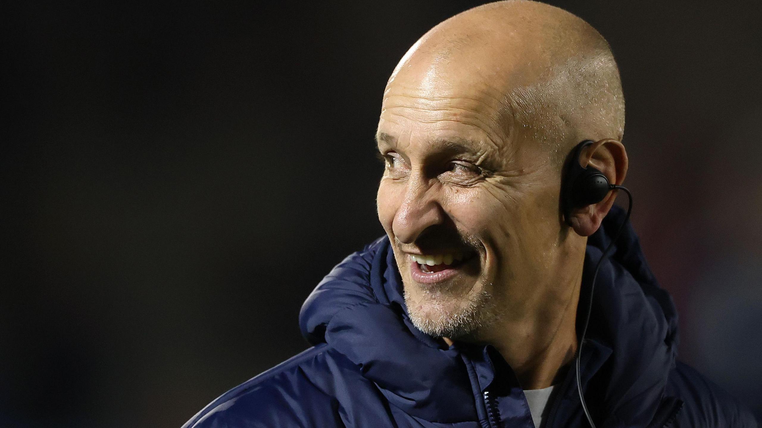 Alan Dickens wearing an ear piece in his left ear, looking to his right and with a smile on his face, ahead of the recent match at Sale