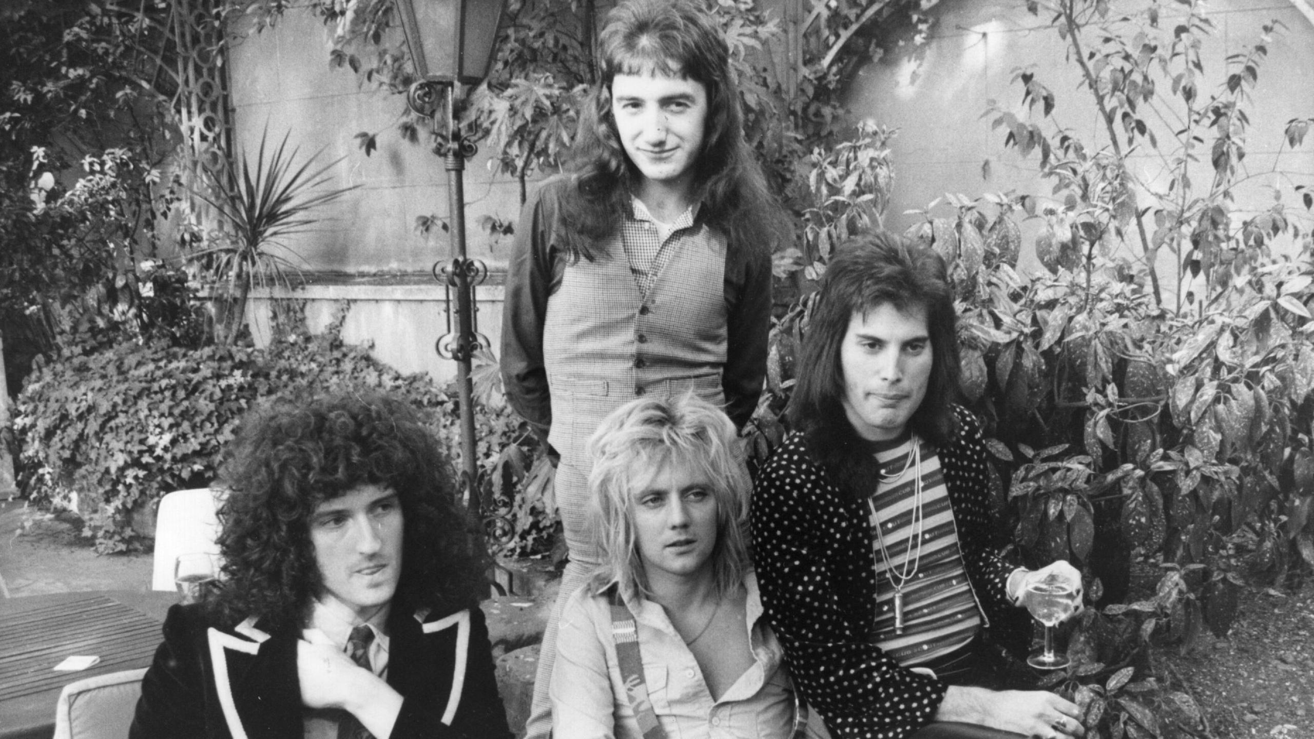 Black and white photograph of rock band Queen sat in a courtyard