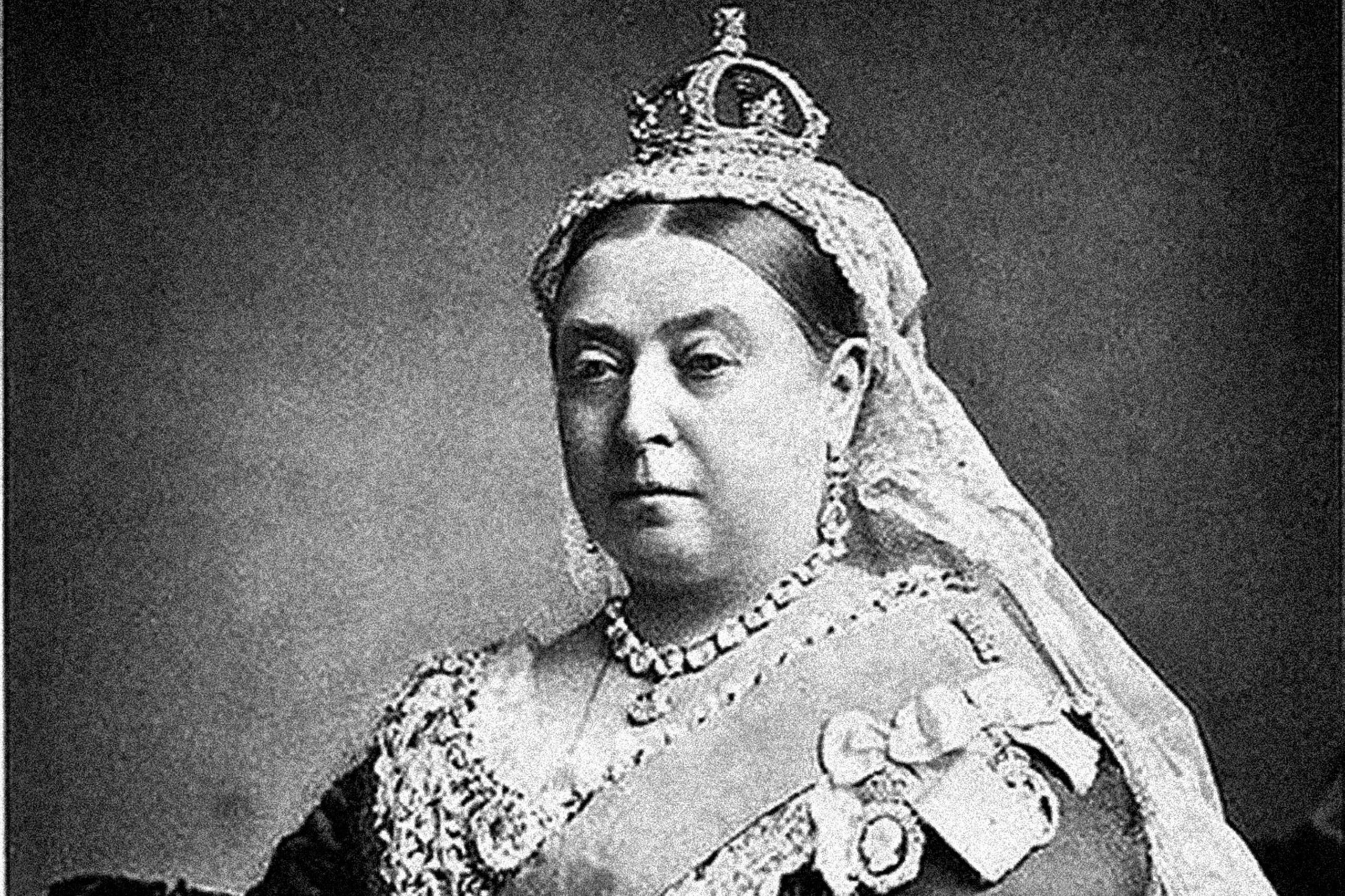 Black and white picture of Queen Victoria. She is wearing a crown with a veil hanging down from the back of it. She is wearing a thick necklace and a v-necked dress.