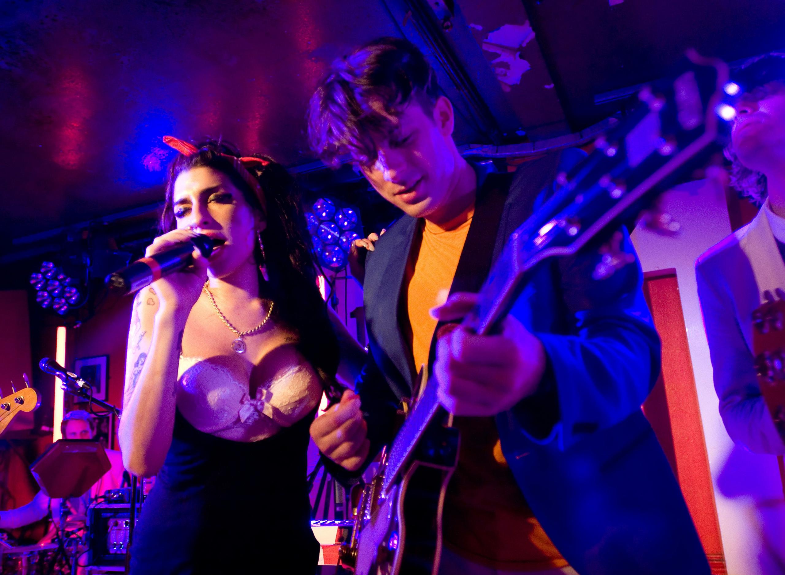 Mark Ronson playing guitar next to Amy Winehouse singing into a microphone on stage