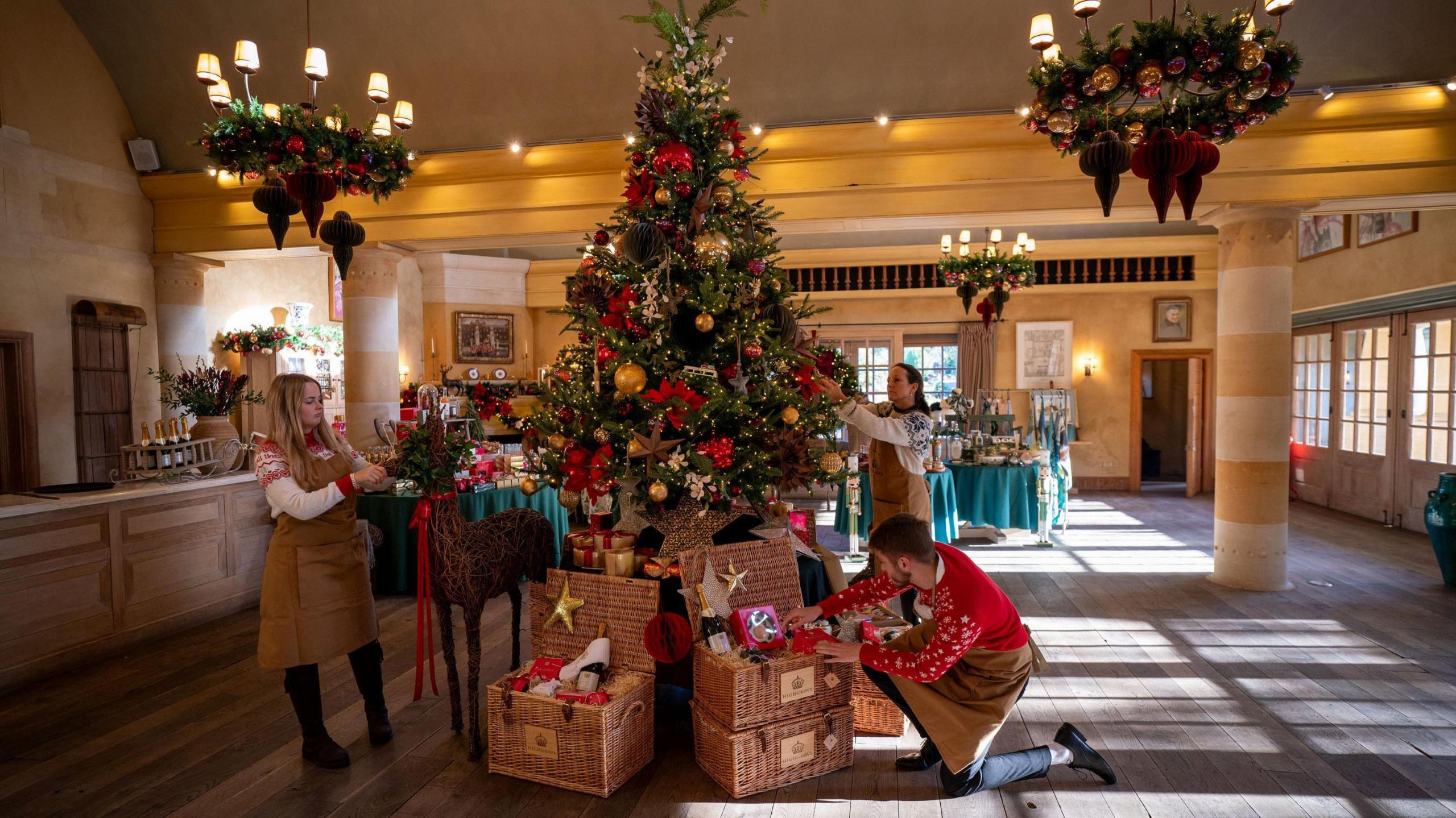 Highgrove staff place presents under the Christmas tree in the Orchard Room, the function suite at Highgrove in Gloucestershire. The staff are all wearing brown aprons and Christmas jumpers