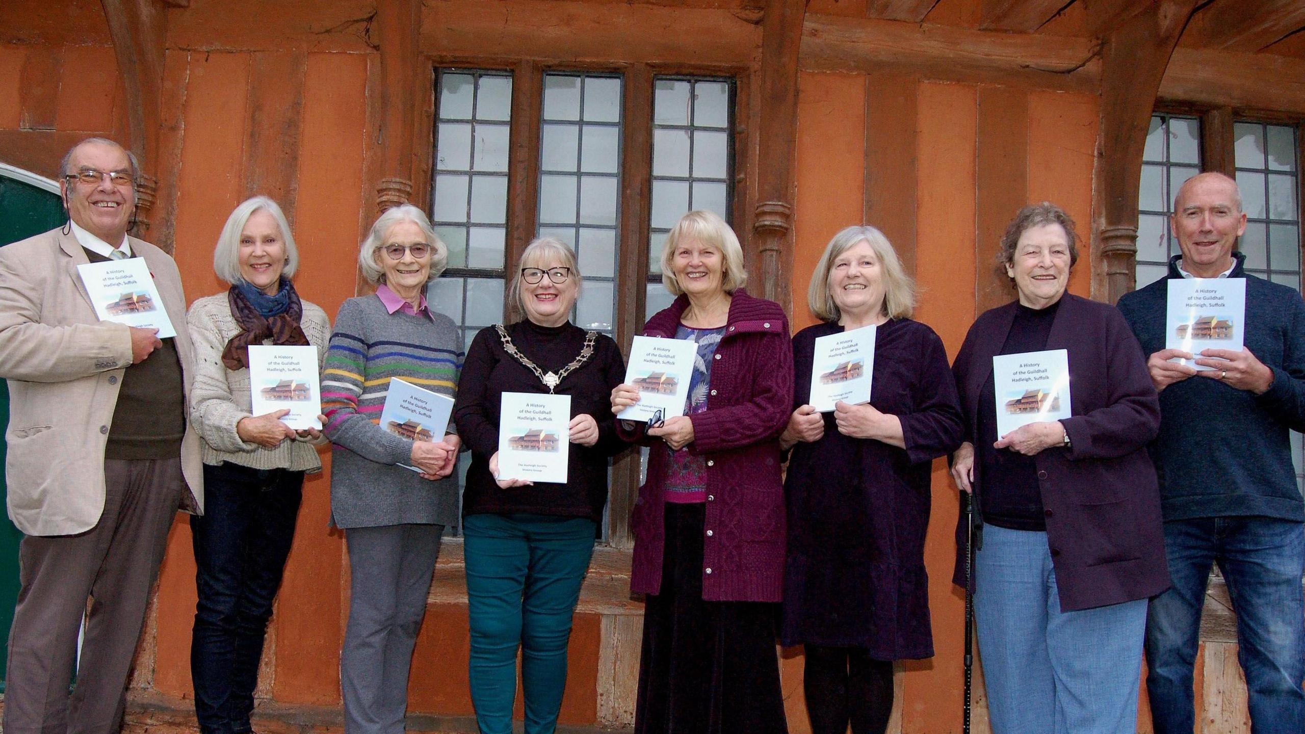 The Hadleigh Society History Group authors stand in a line holding their new book in front of the Guildhall building. They are looking at the camera and smiling. 